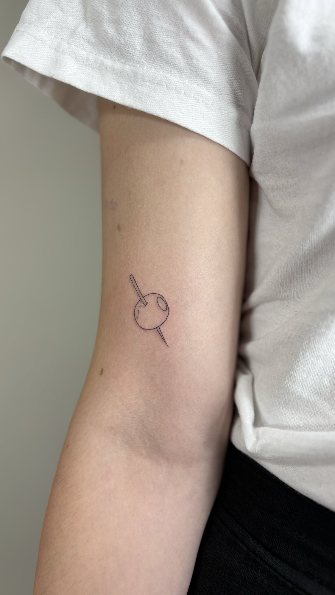 Tatuaje de aguja atravesando boton en brazo, línea fina