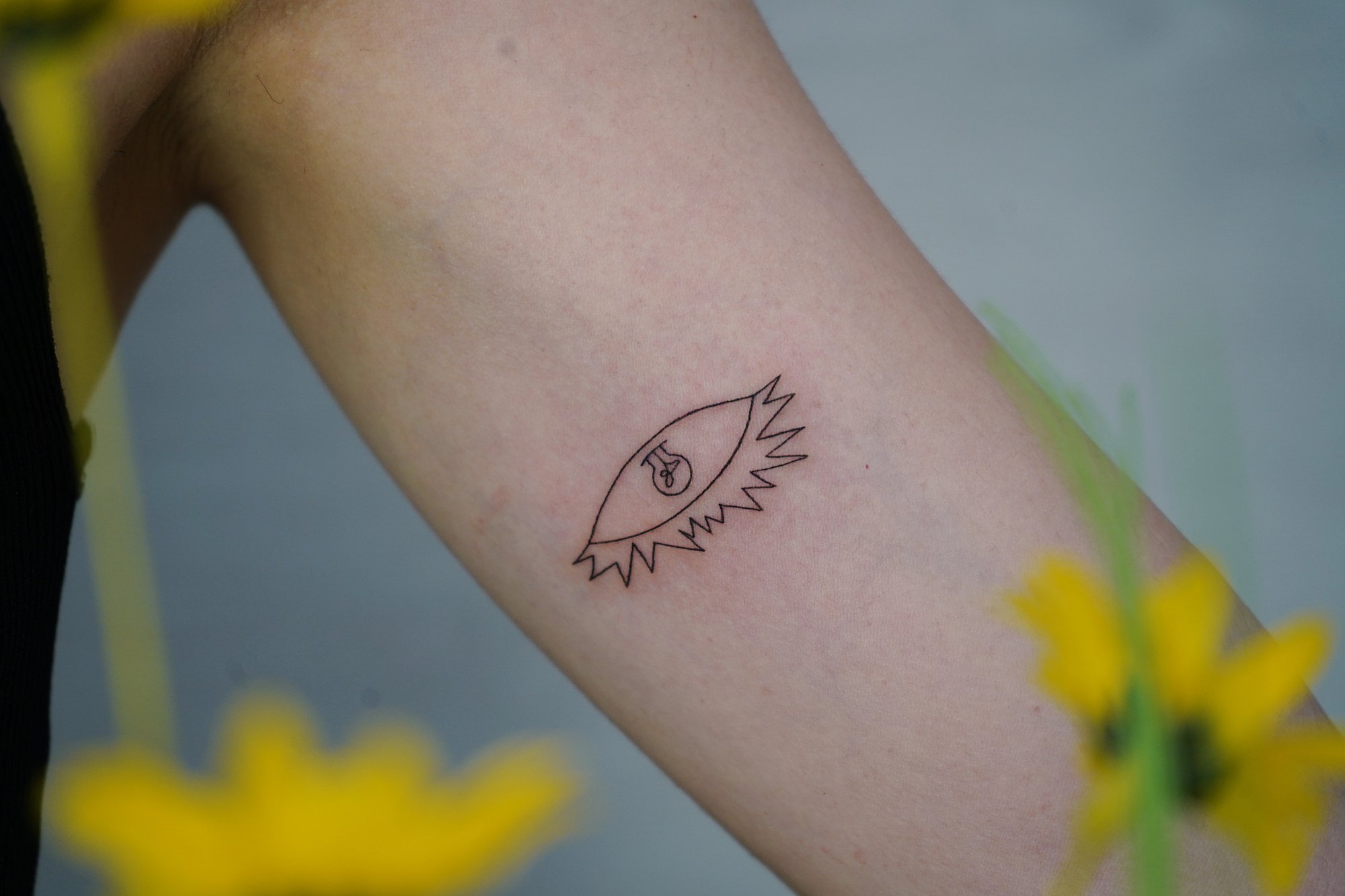 Tatuaje de bombilla ojo en biceps, línea fina