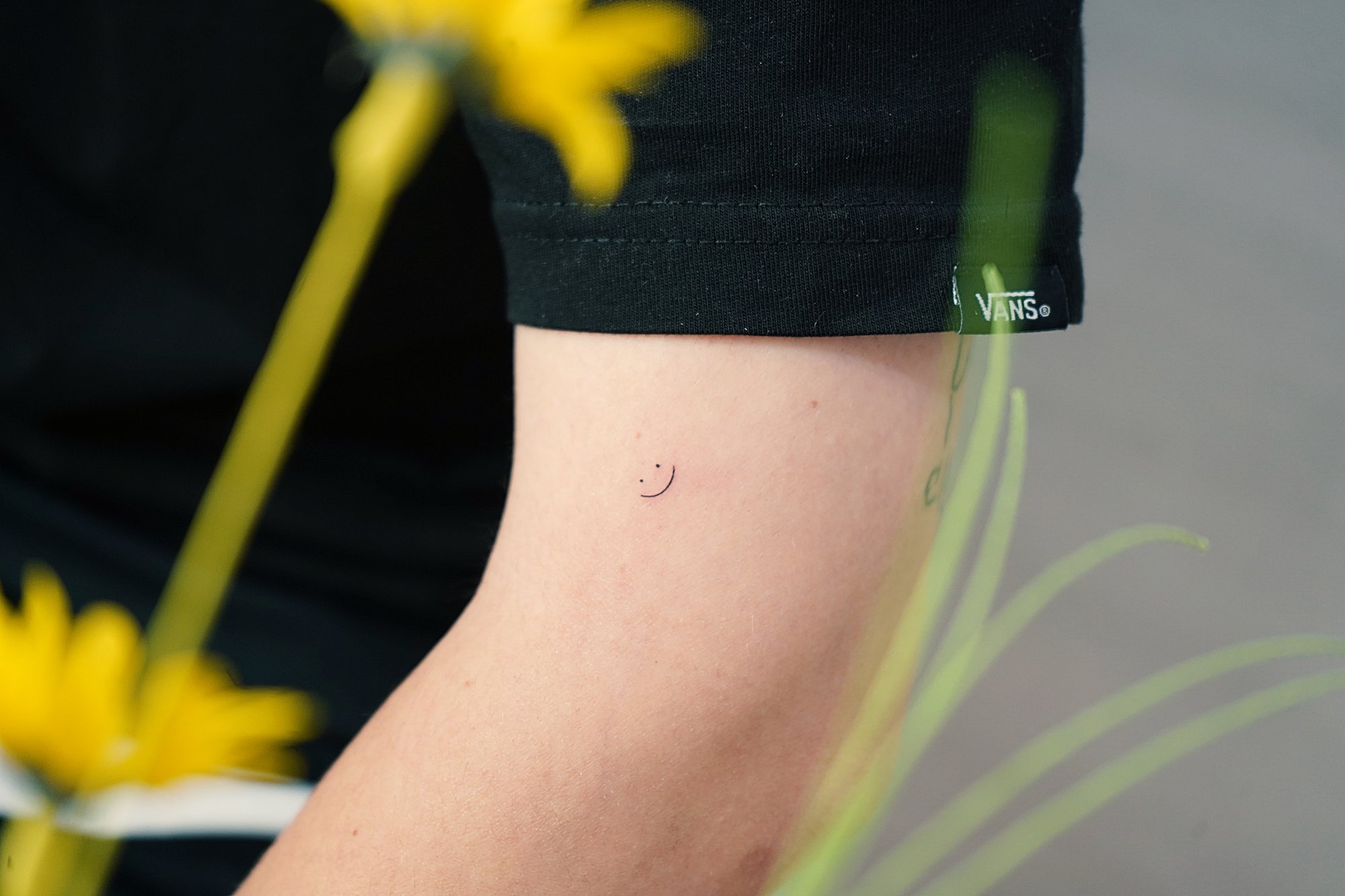 Tatuaje de carita feliz en brazo, línea fina