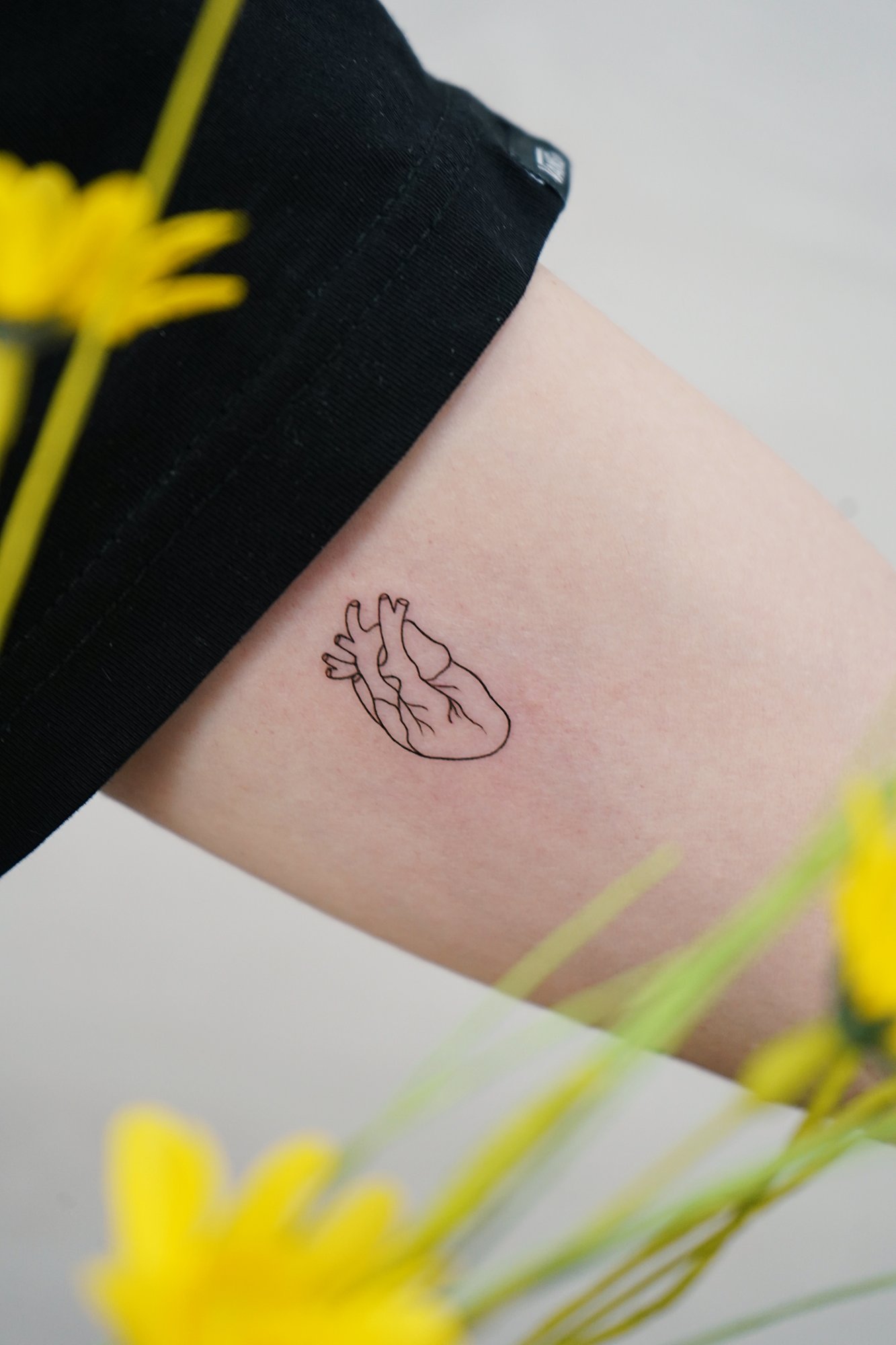 Tatuaje de corazon lineal en brazo, línea fina