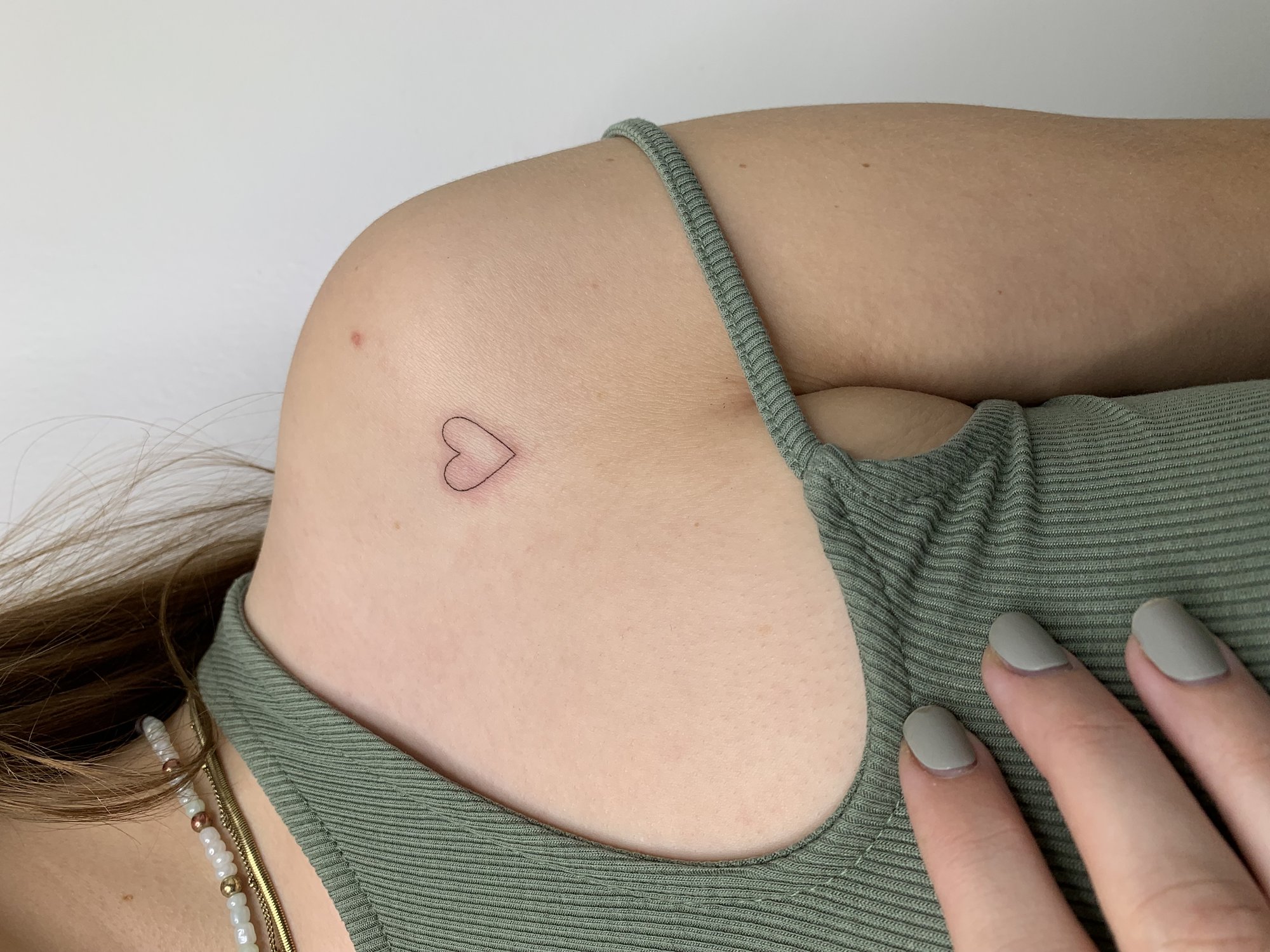 Tatuaje de corazon pequeno rosa delicado en hombro, línea fina