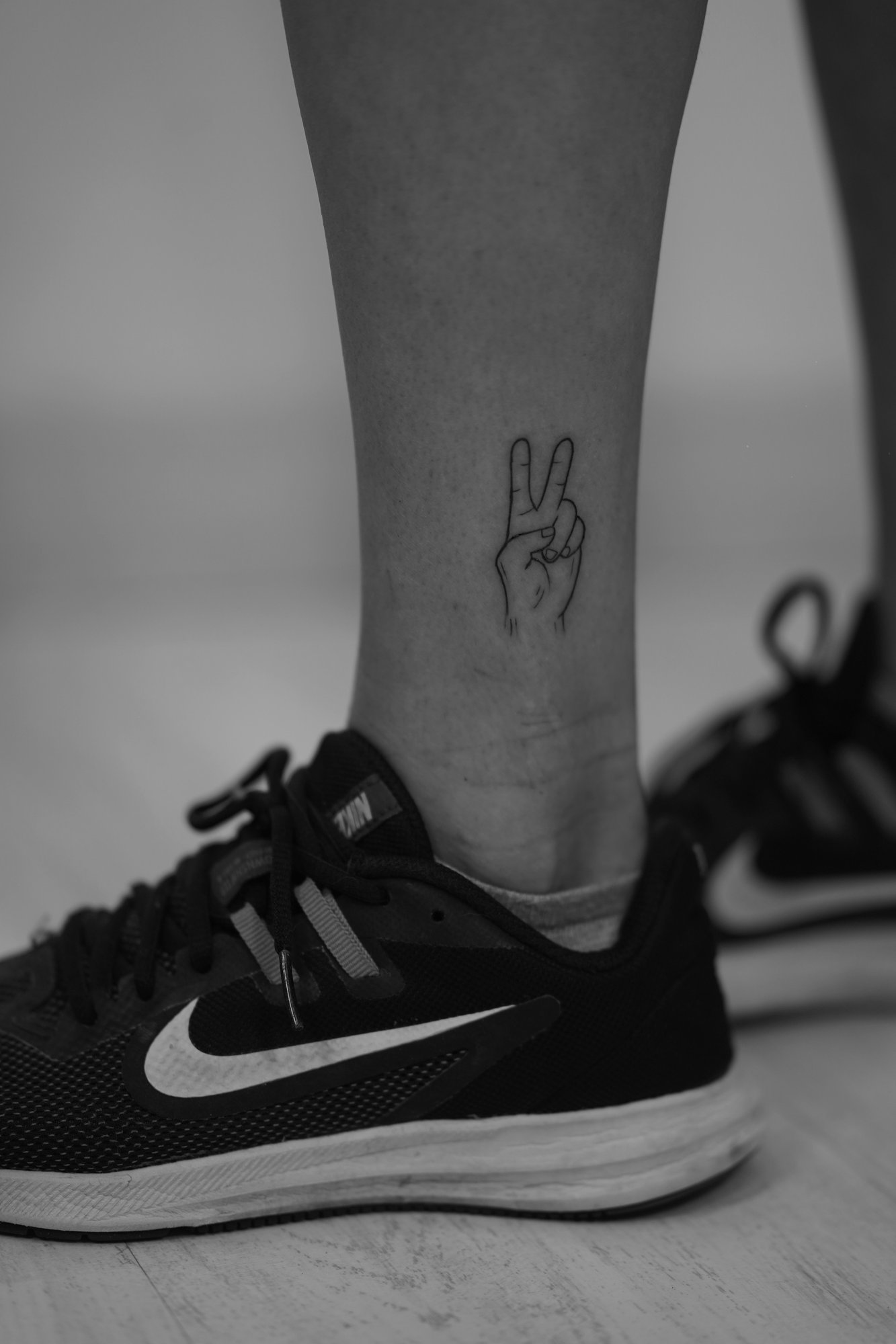 Tatuaje de mano senal de paz en tobillo, línea fina