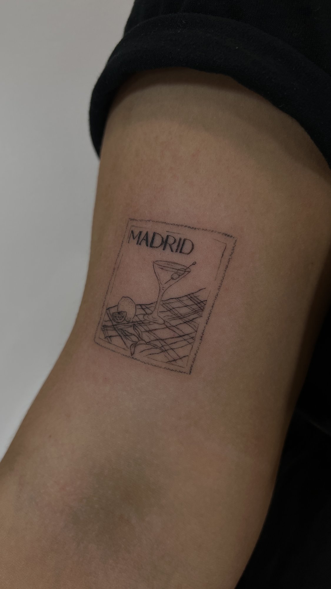 Tatuaje de sello postal madrid coctel en brazo, línea fina