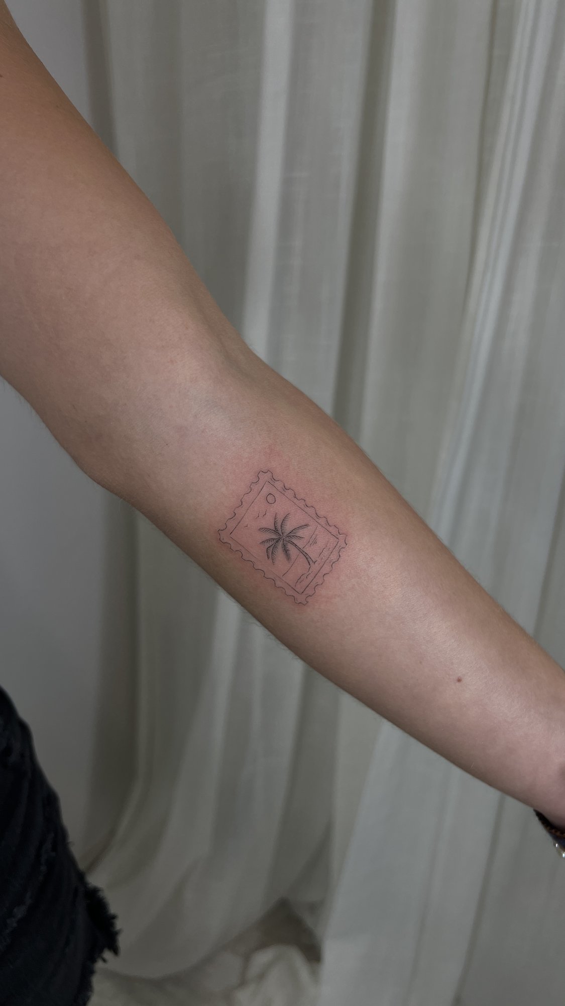 Tatuaje de sello postal palmera playa en antebrazo, línea fina