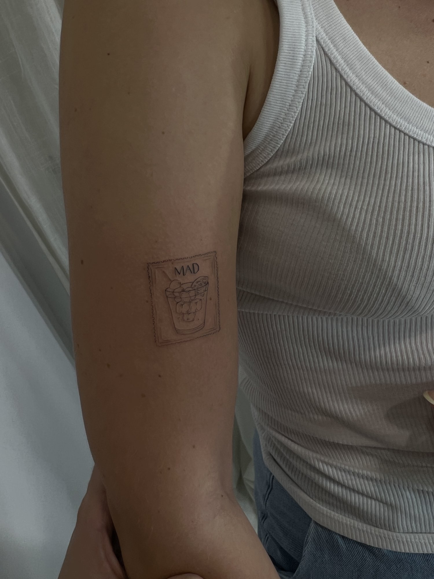 Tatuaje de sello postal vaso cocktail mad en brazo, línea fina