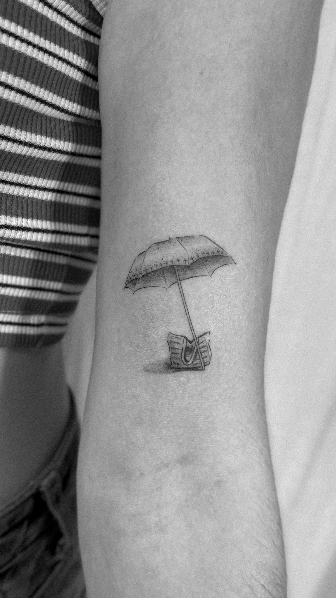 Tatuaje de sombrilla con silla playa en brazo, línea fina