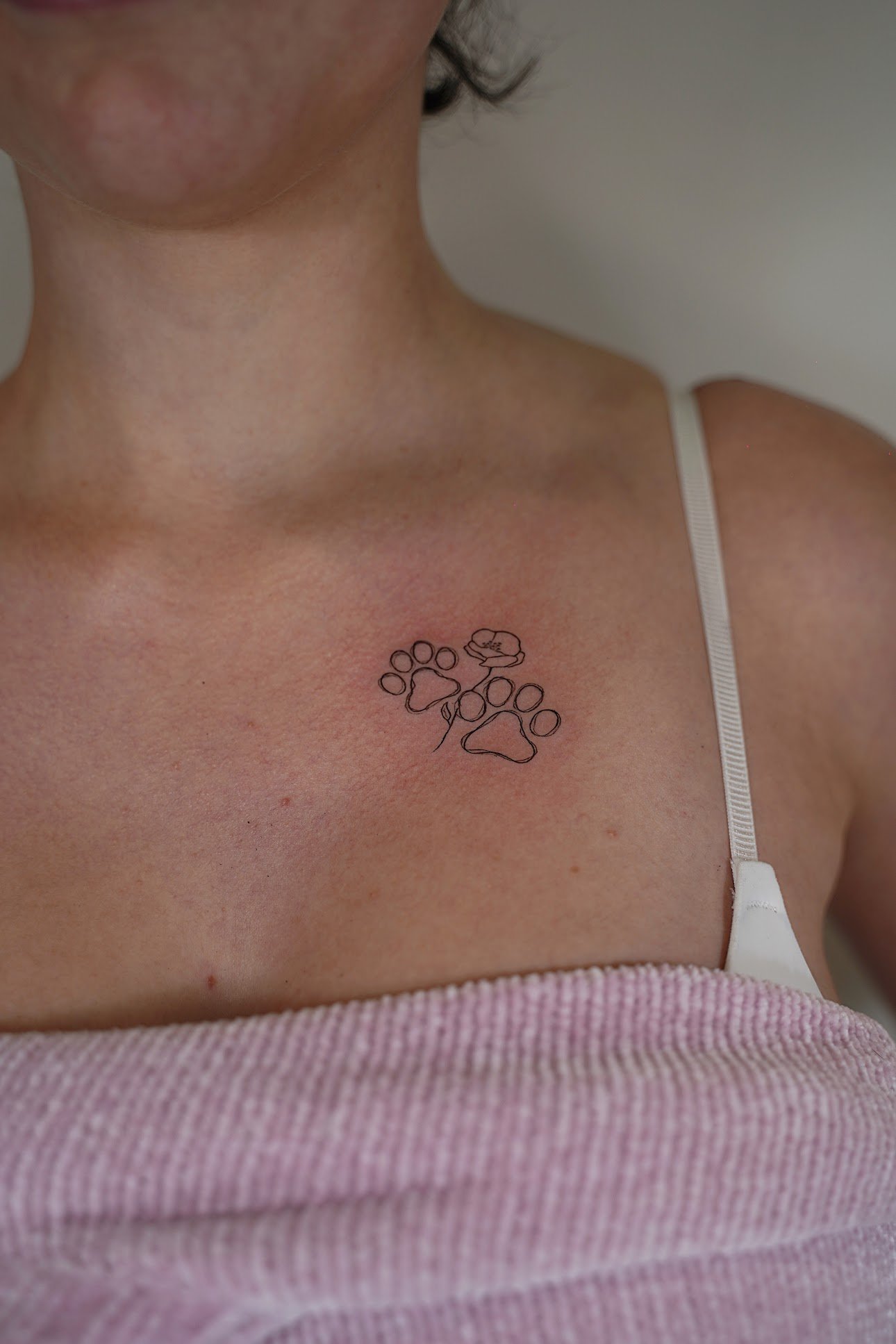 Tatuaje de huellas patitas con flor en pecho, línea fina
