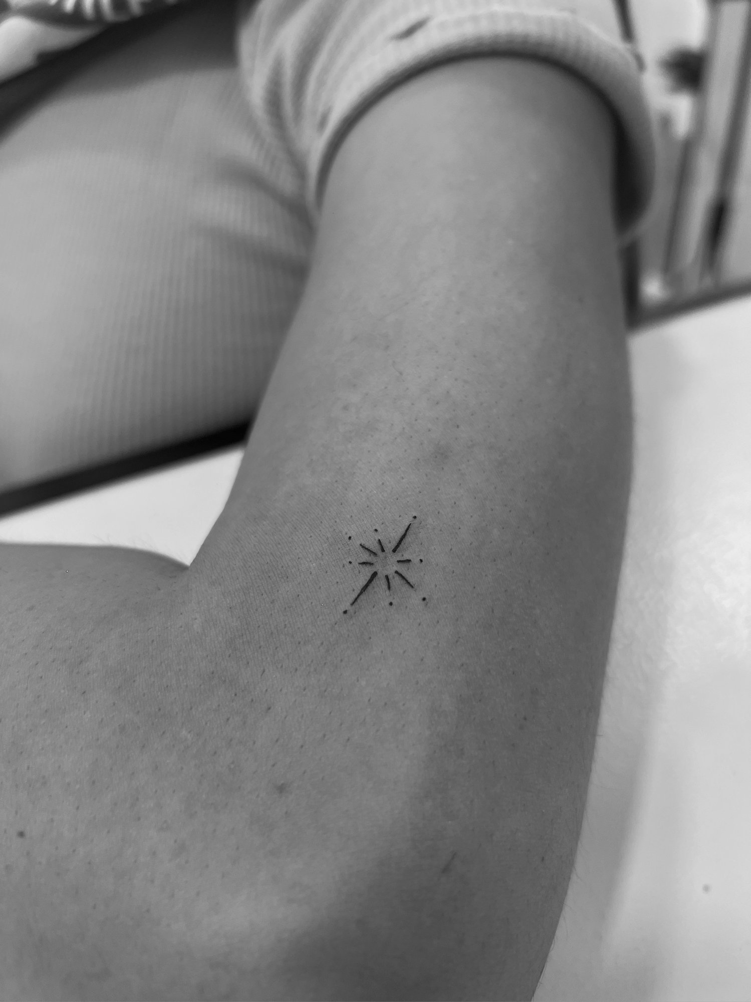 Tatuaje de estrella con destellos minimal en brazo, línea fina