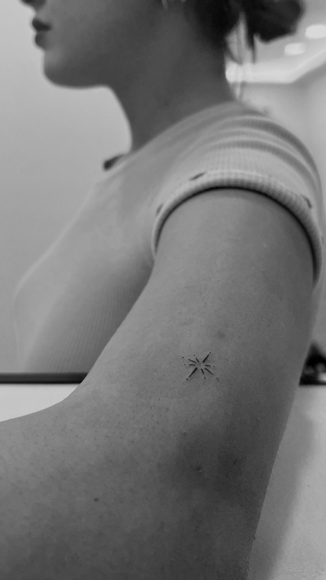Tatuaje de estrella pequena con destellos en brazo, línea fina