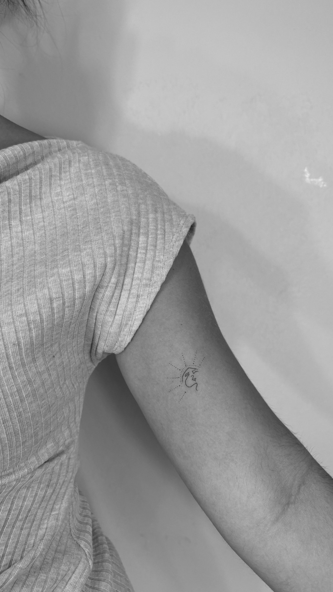 Tatuaje de sol con cara abstracta en brazo, línea fina