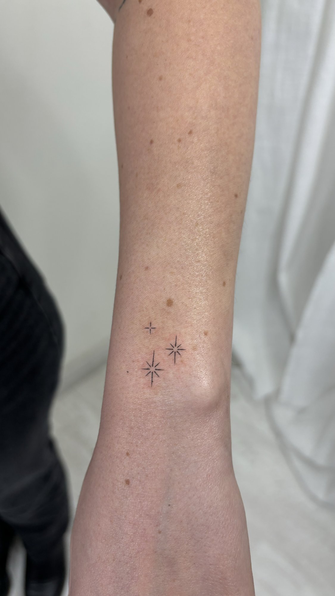 Tatuaje de tres estrellas brillantes mini en antebrazo, línea fina