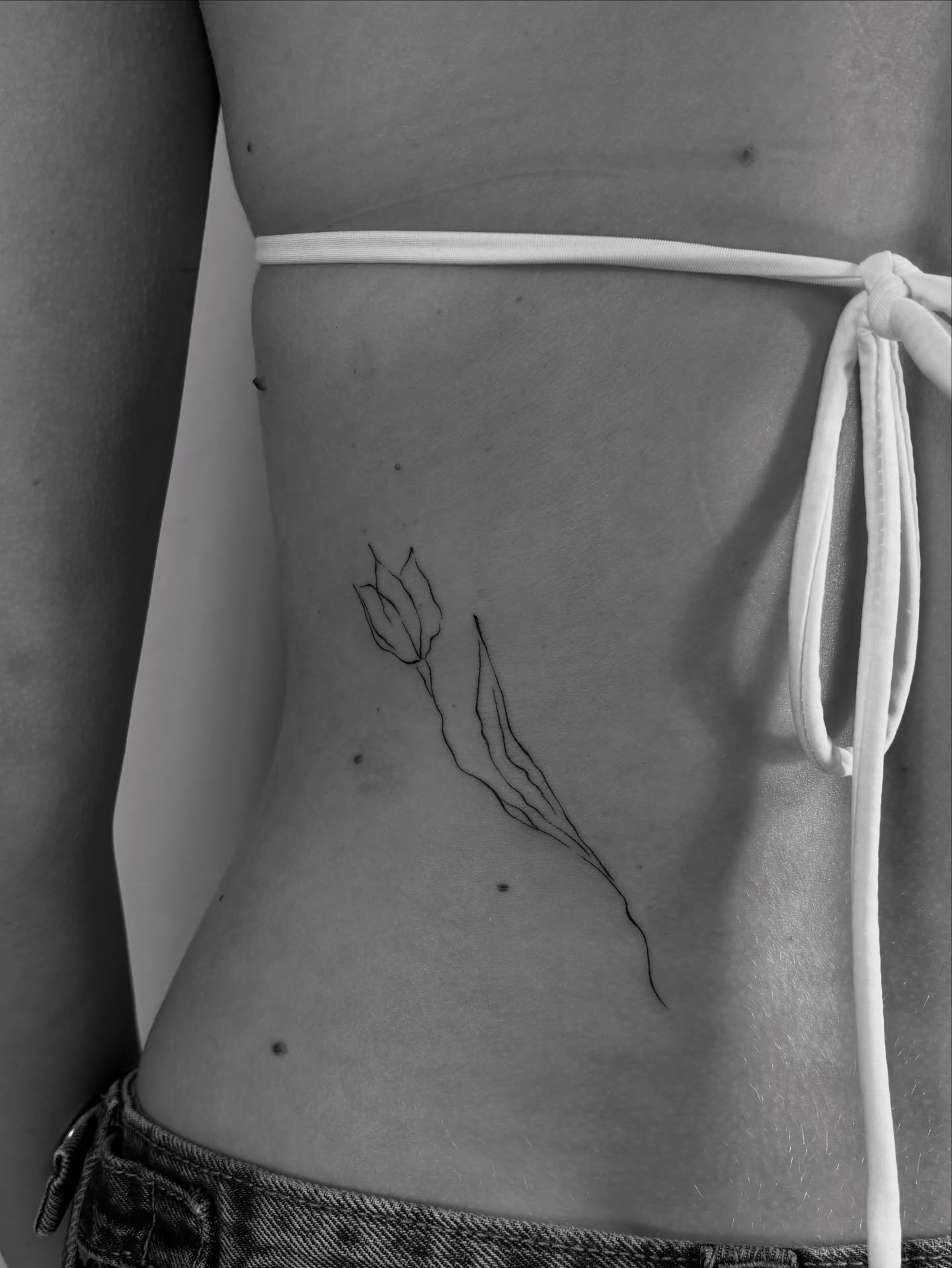 Tatuaje de flor en costilla, línea fina Sinkply Madrid