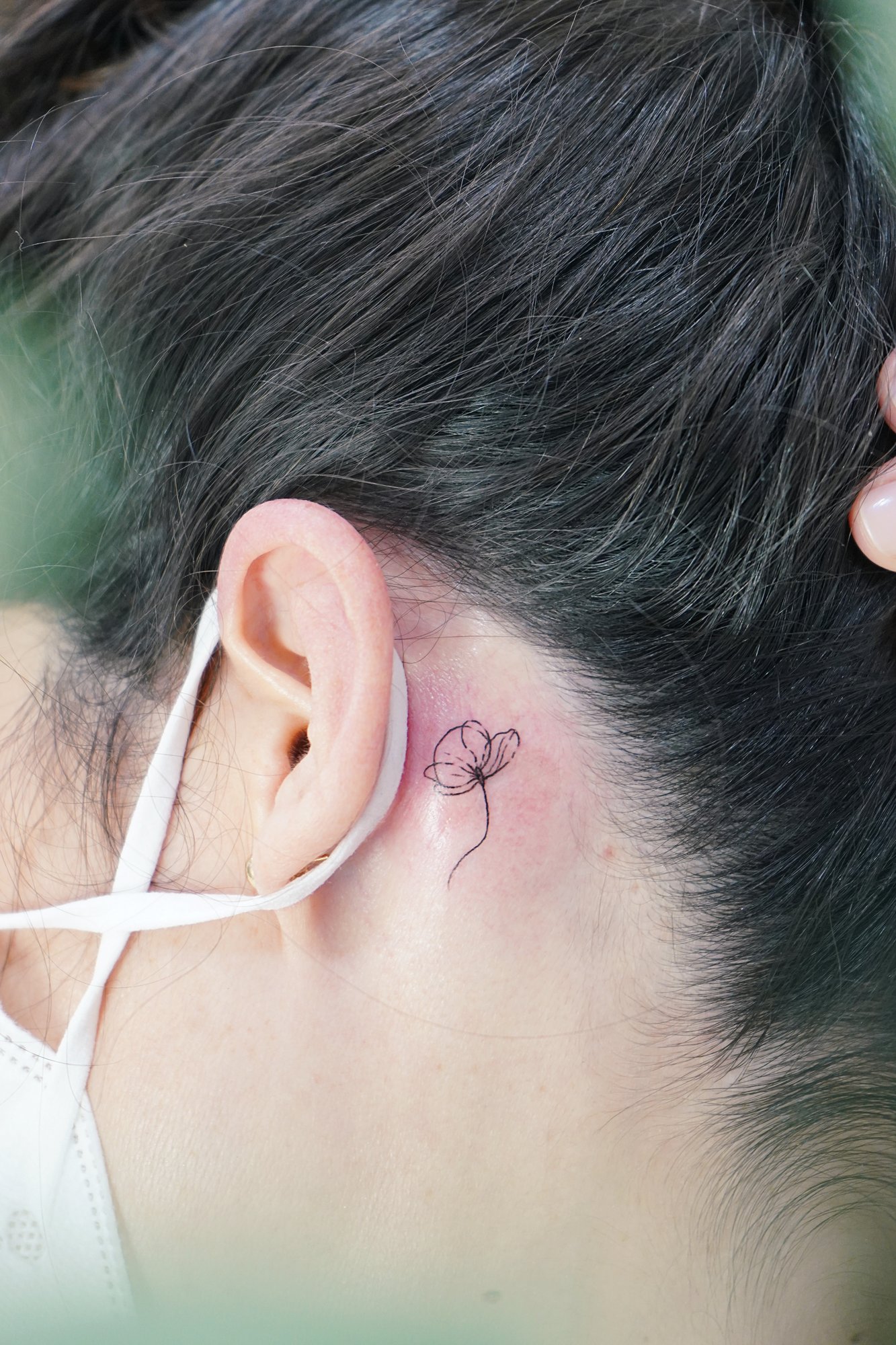Tatuaje de flor en detras oreja, línea fina