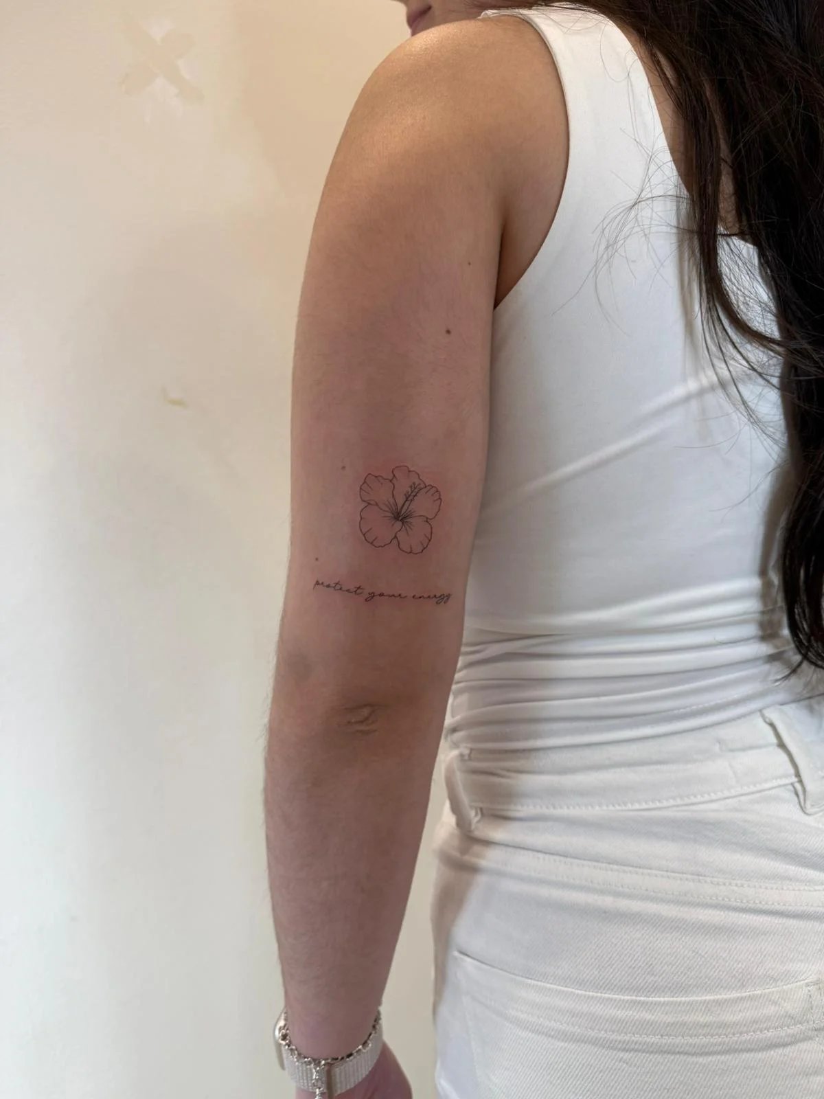 Tatuaje floral hibisco con frase cursiva antebrazo