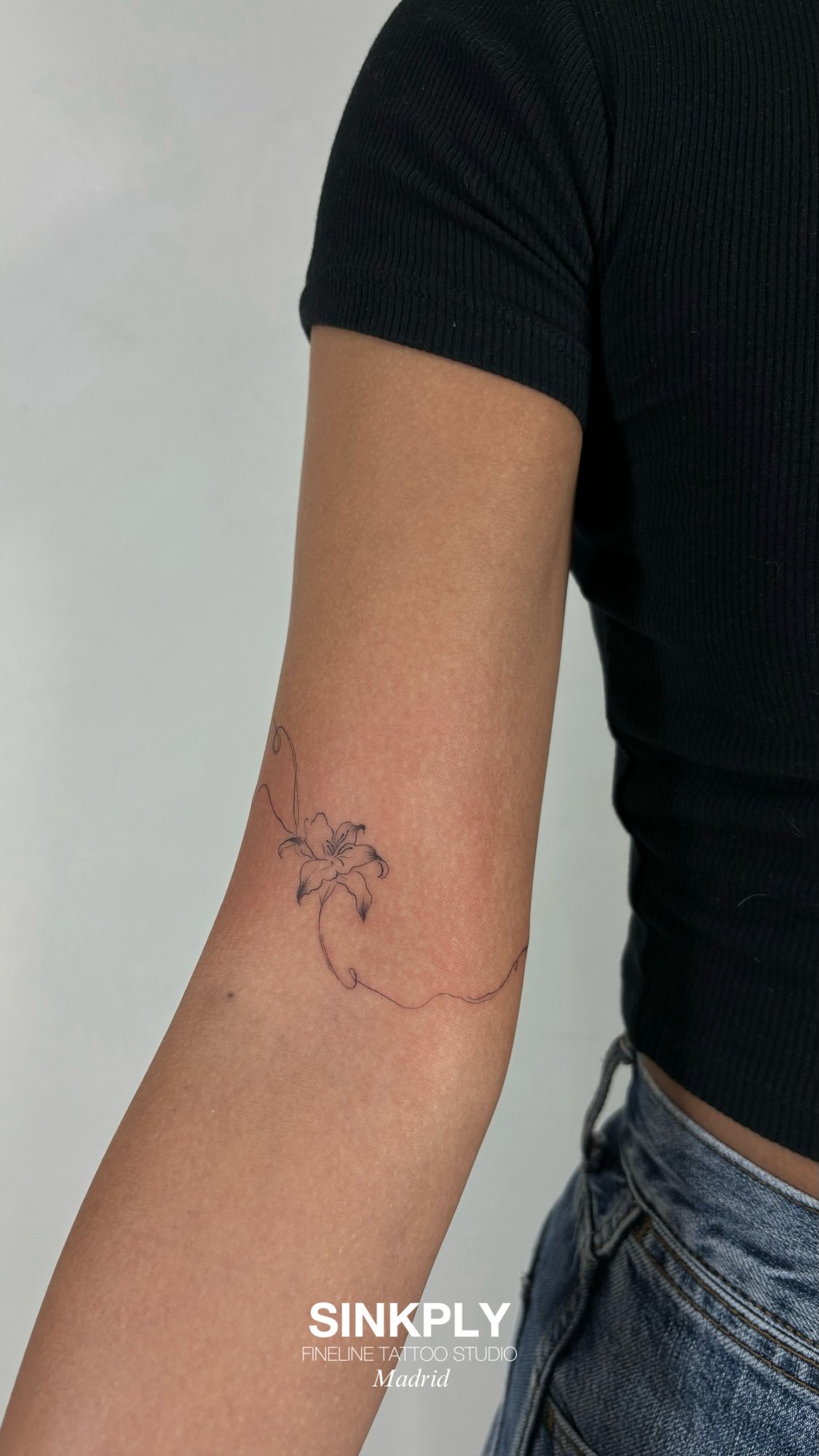 Tatuaje de lirio fineline con tallo en brazo, línea fina