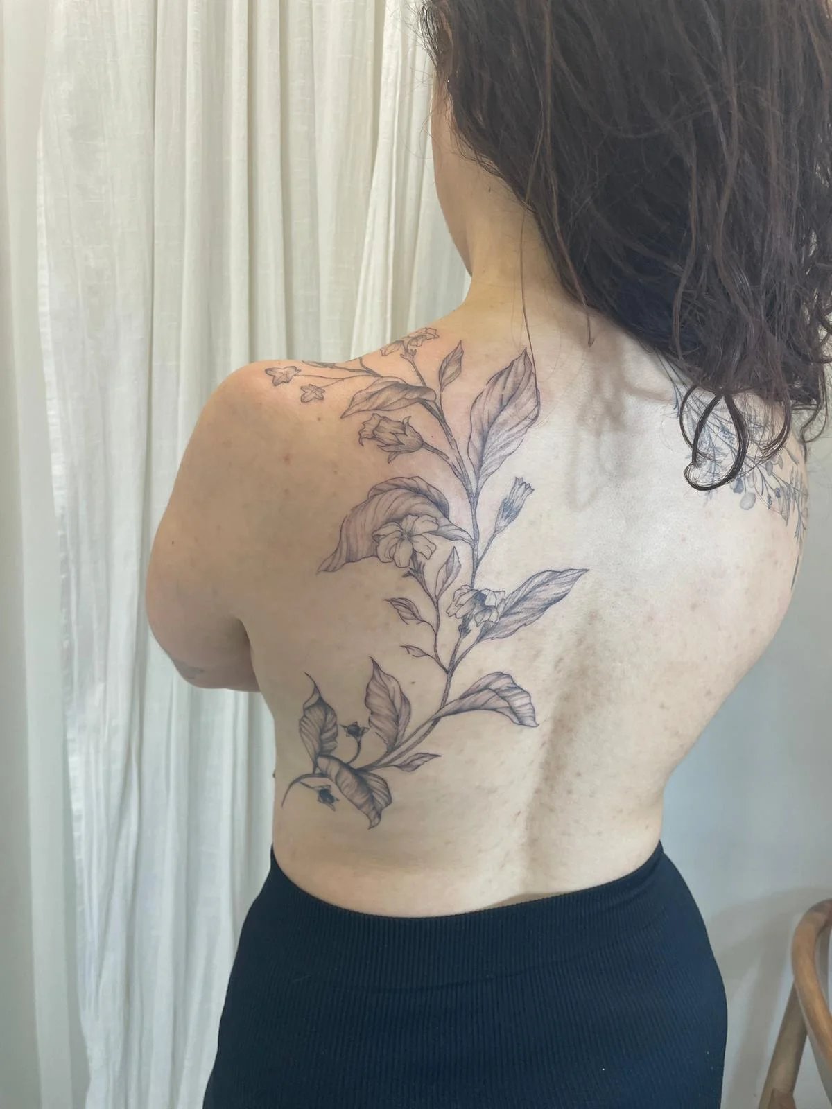 Tatuaje floral fine line espalda con ramas y hojas botanicas delicadas