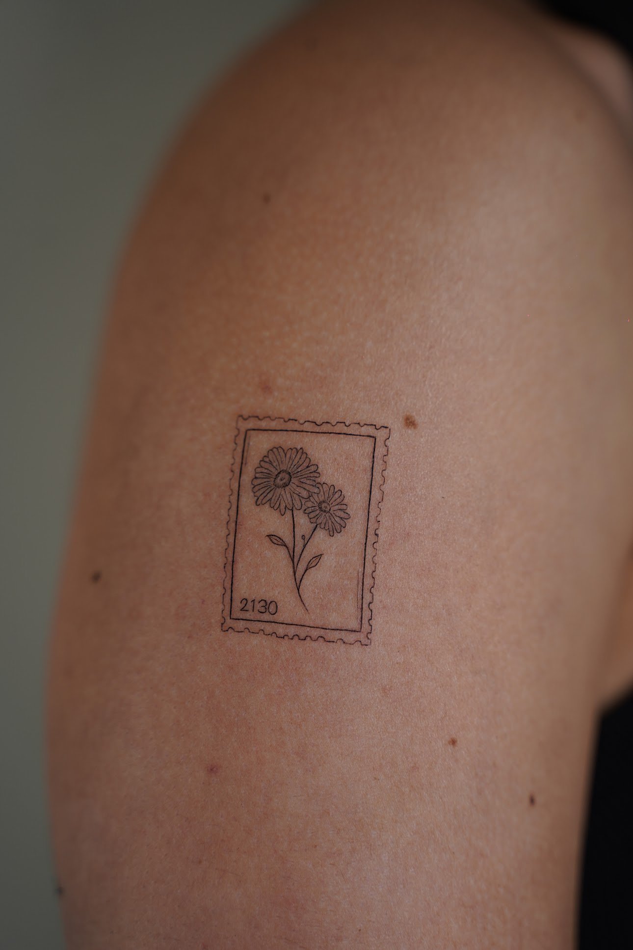 Tatuaje de sello postal con margaritas en brazo, línea fina