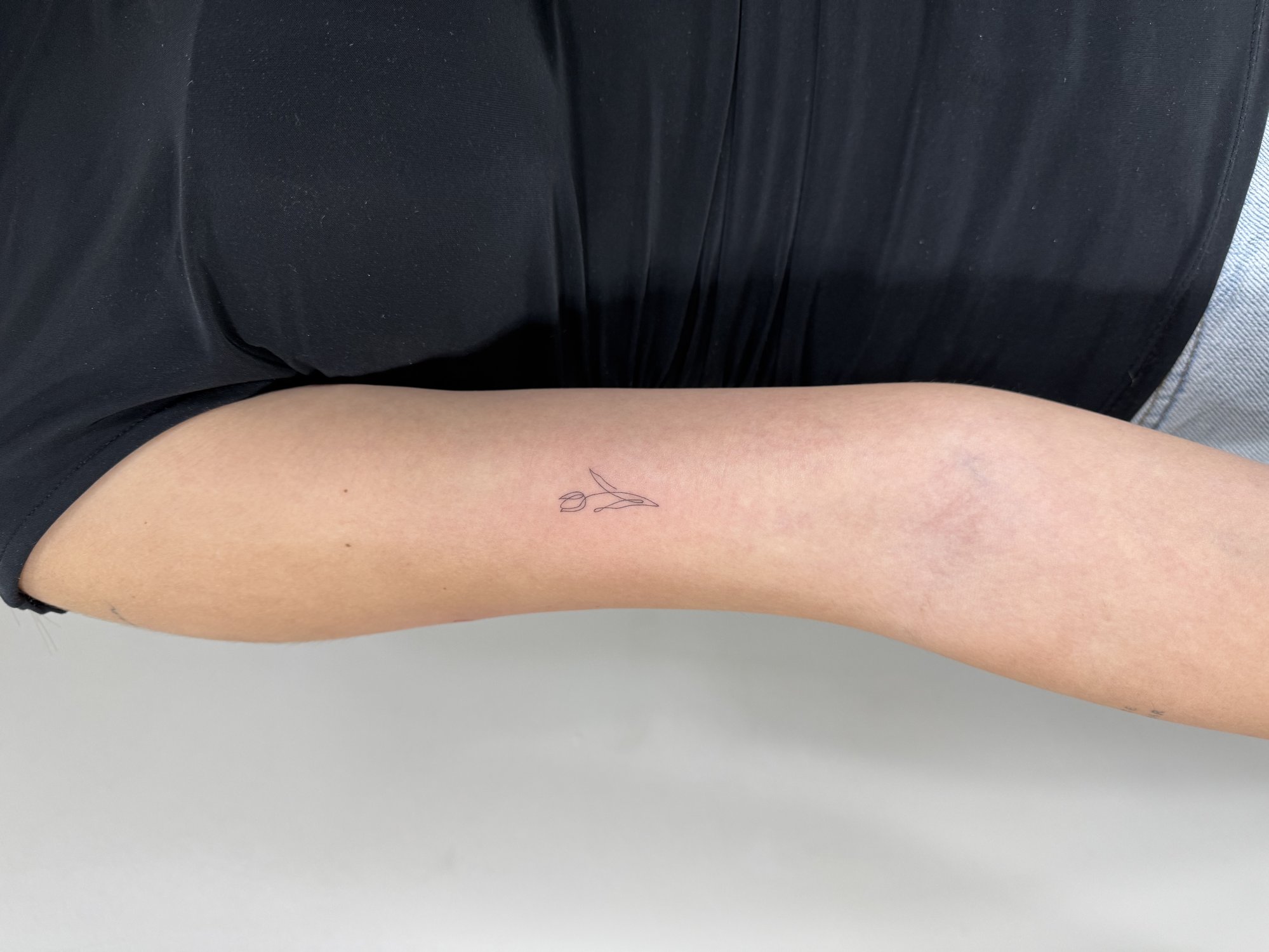 Tatuaje de tulipan minimalista linea fina en brazo, línea fina