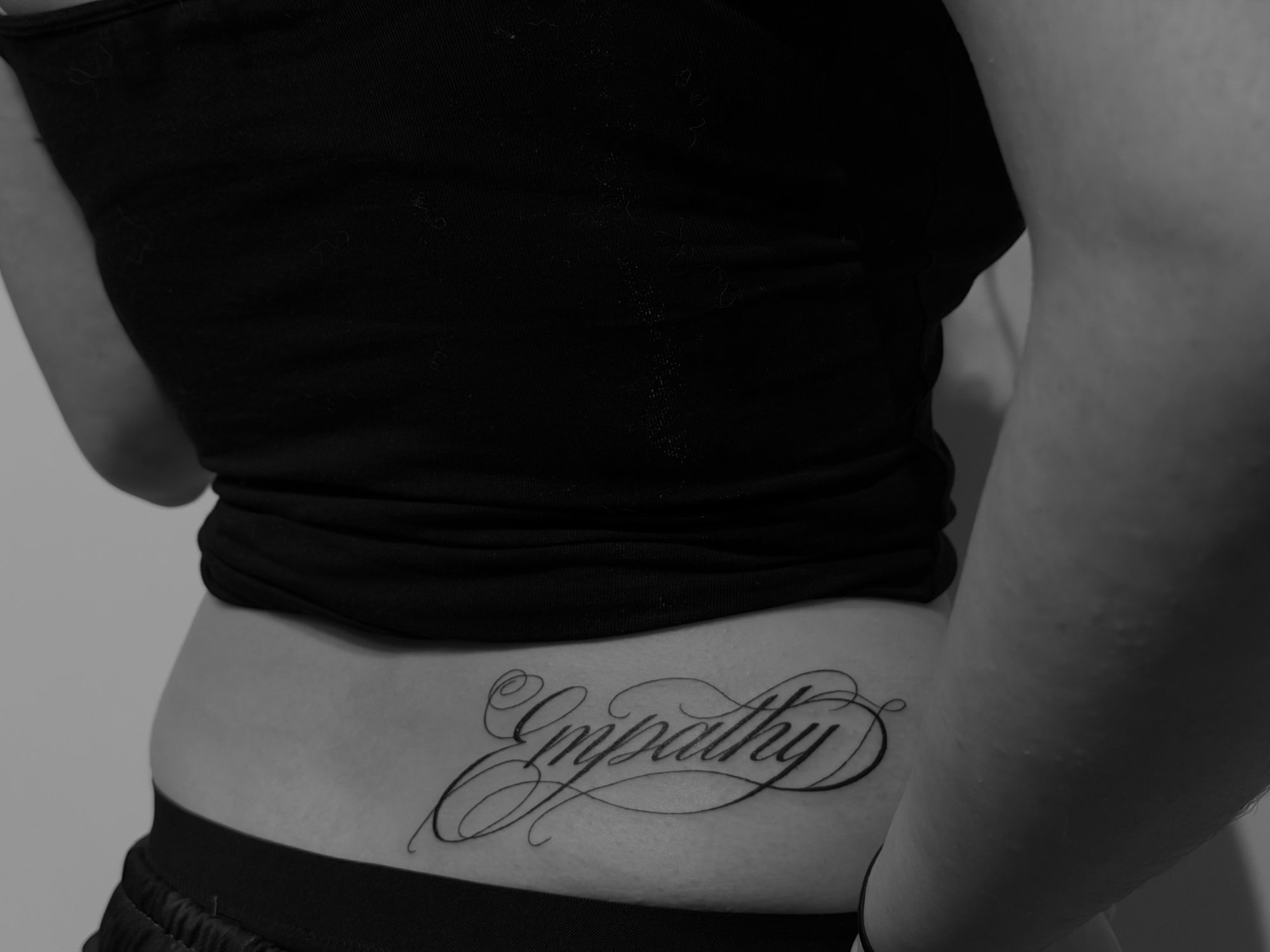 Tatuaje de empathy caligrafia cursiva ele en espalda, línea fina