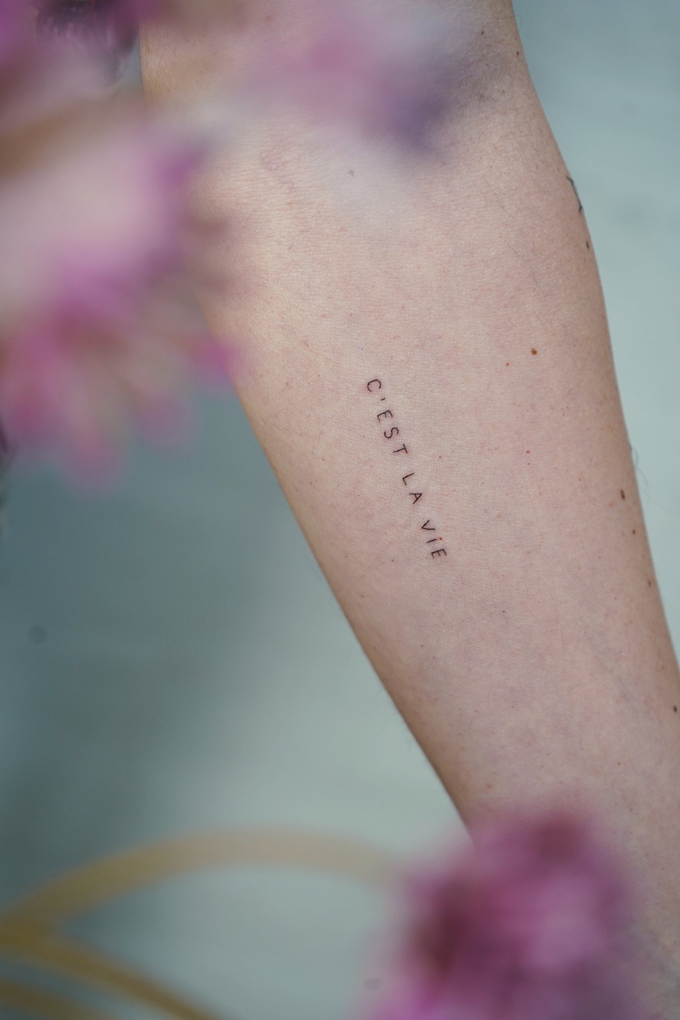 Tatuaje de frase francesa en brazo, línea fina