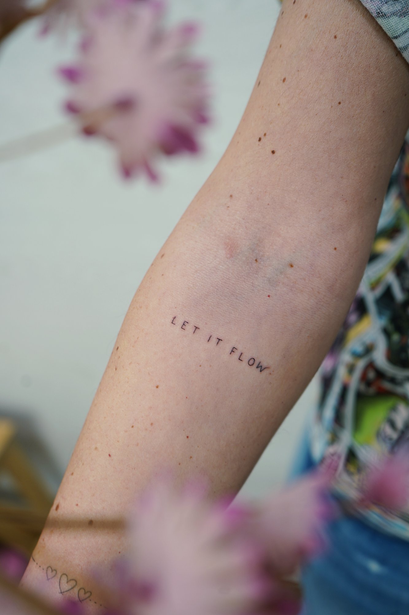 Tatuaje de frase let it flow en brazo, línea fina