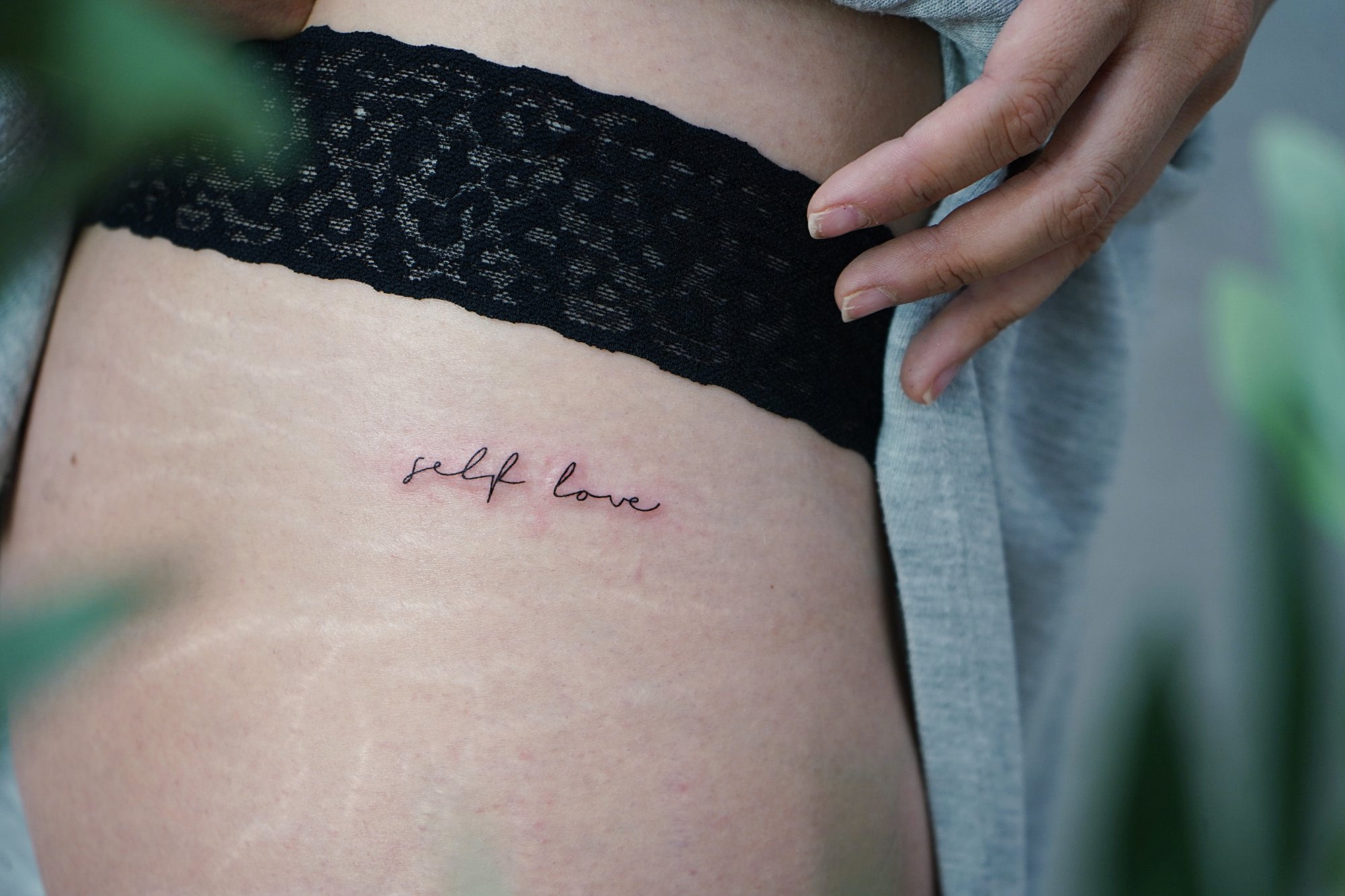 Tatuaje de frase self love en cadera, línea fina