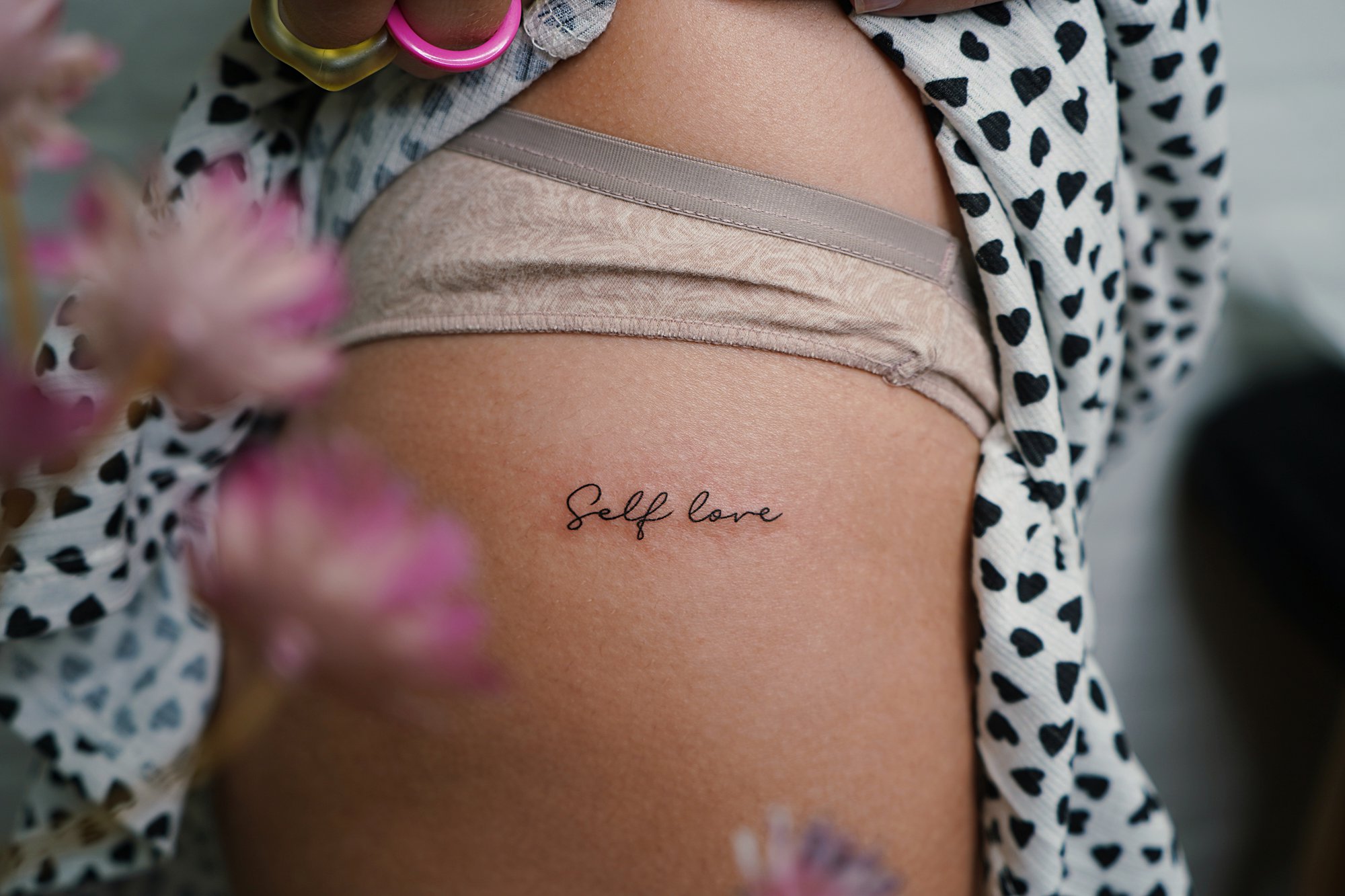 Tatuaje de frase self love en cadera, línea fina