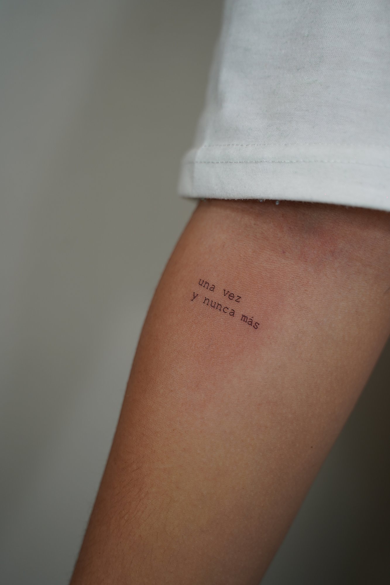 Tatuaje de frase uno mas uno en antebrazo, línea fina