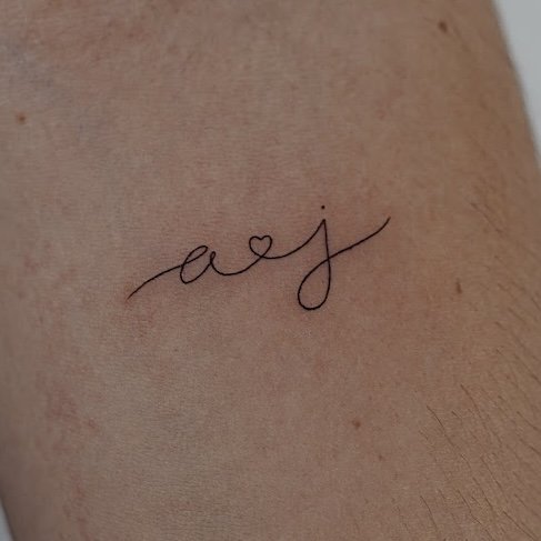 Tatuaje de iniciales a j corazon en antebrazo, línea fina