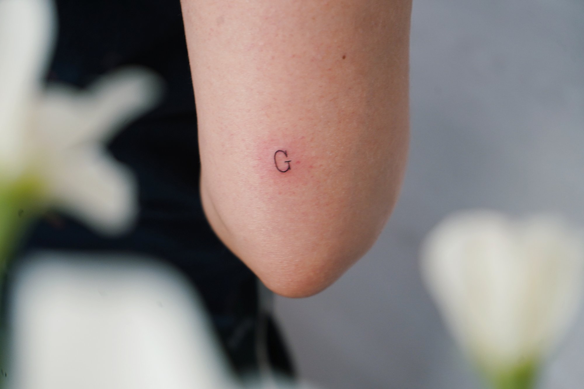 Tatuaje de letra g en codo, línea fina