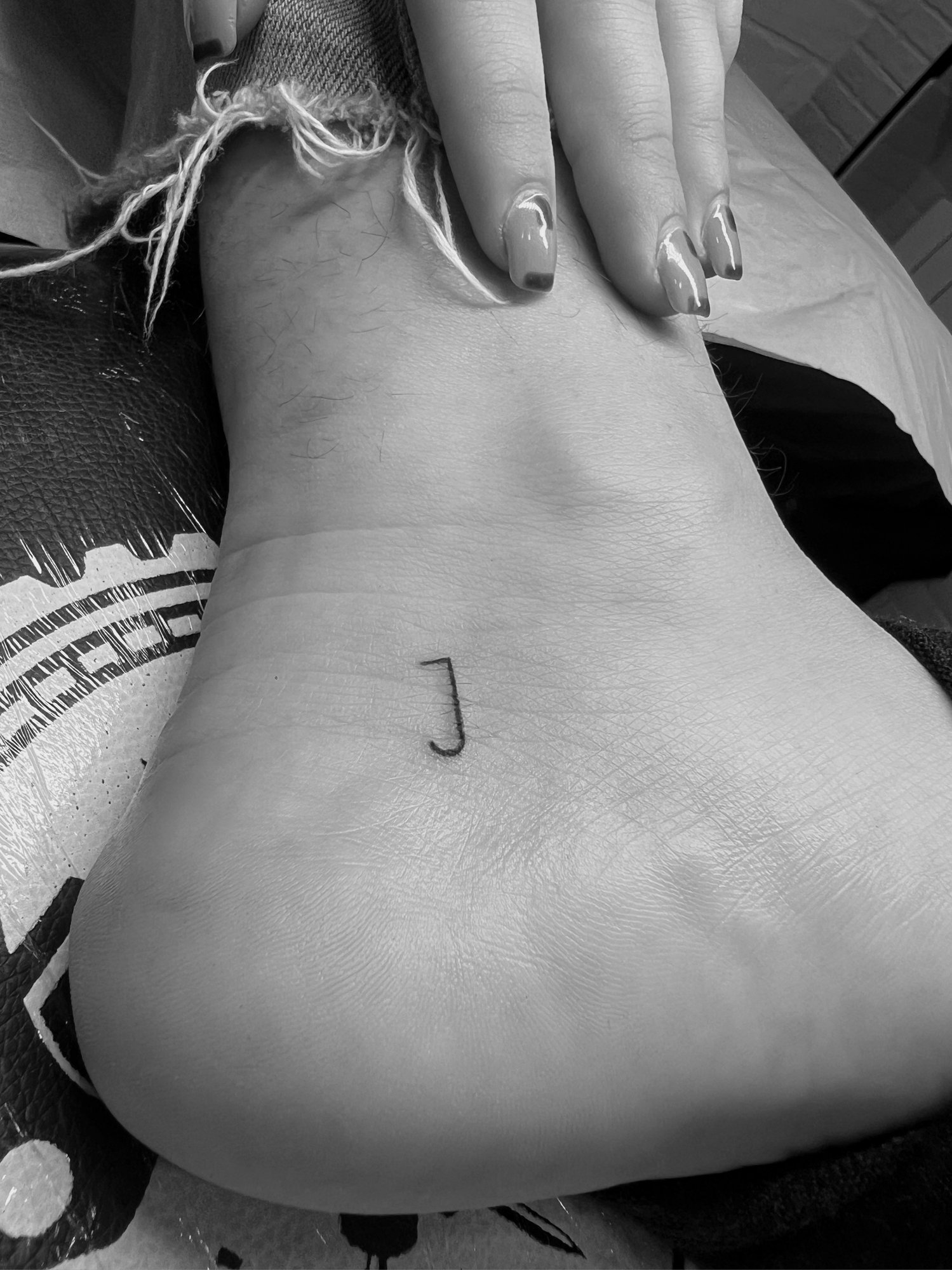 Tatuaje de letra j minimalista en tobillo, línea fina