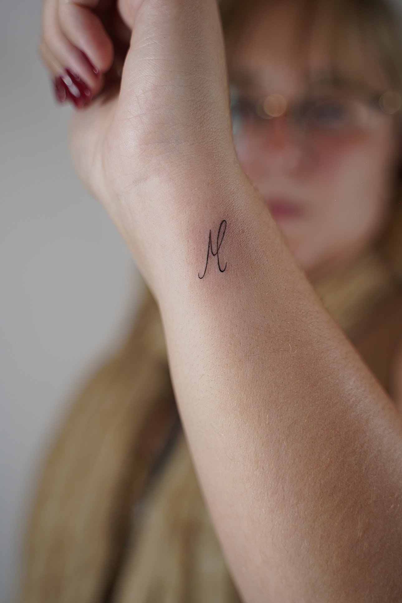 Tatuaje de letra m cursiva elegante en antebrazo, línea fina
