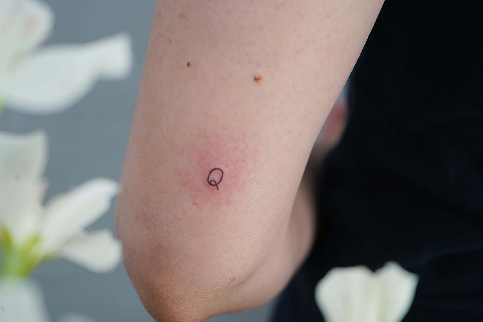 Tatuaje de letra q en codo, línea fina