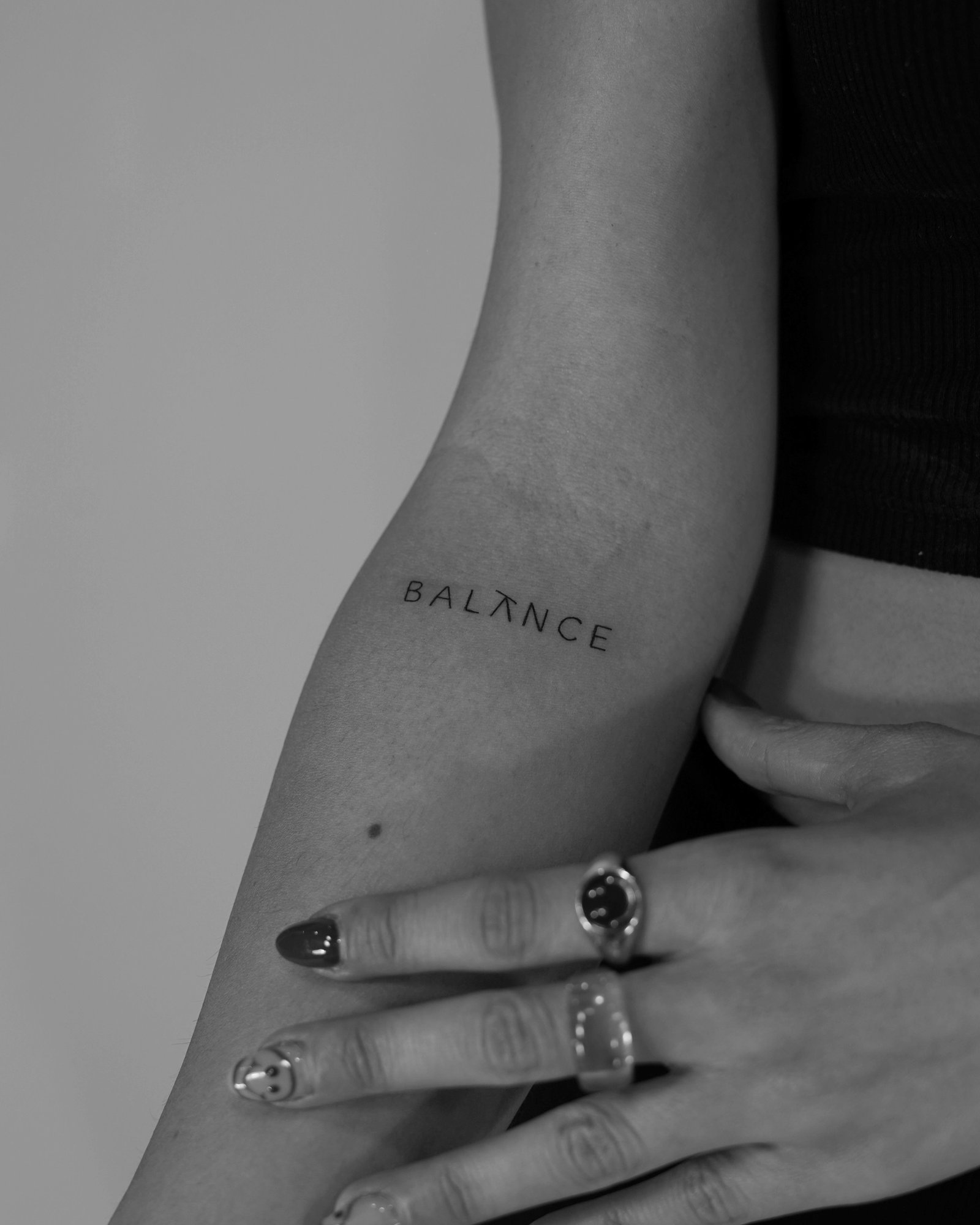 Tatuaje de palabra balance tipografia min en antebrazo, línea fina