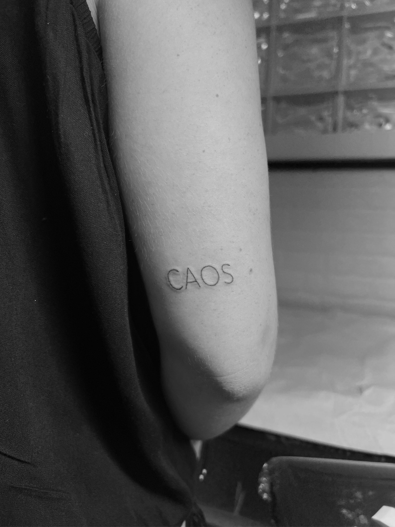 Tatuaje de palabra caos minimalista en antebrazo, línea fina