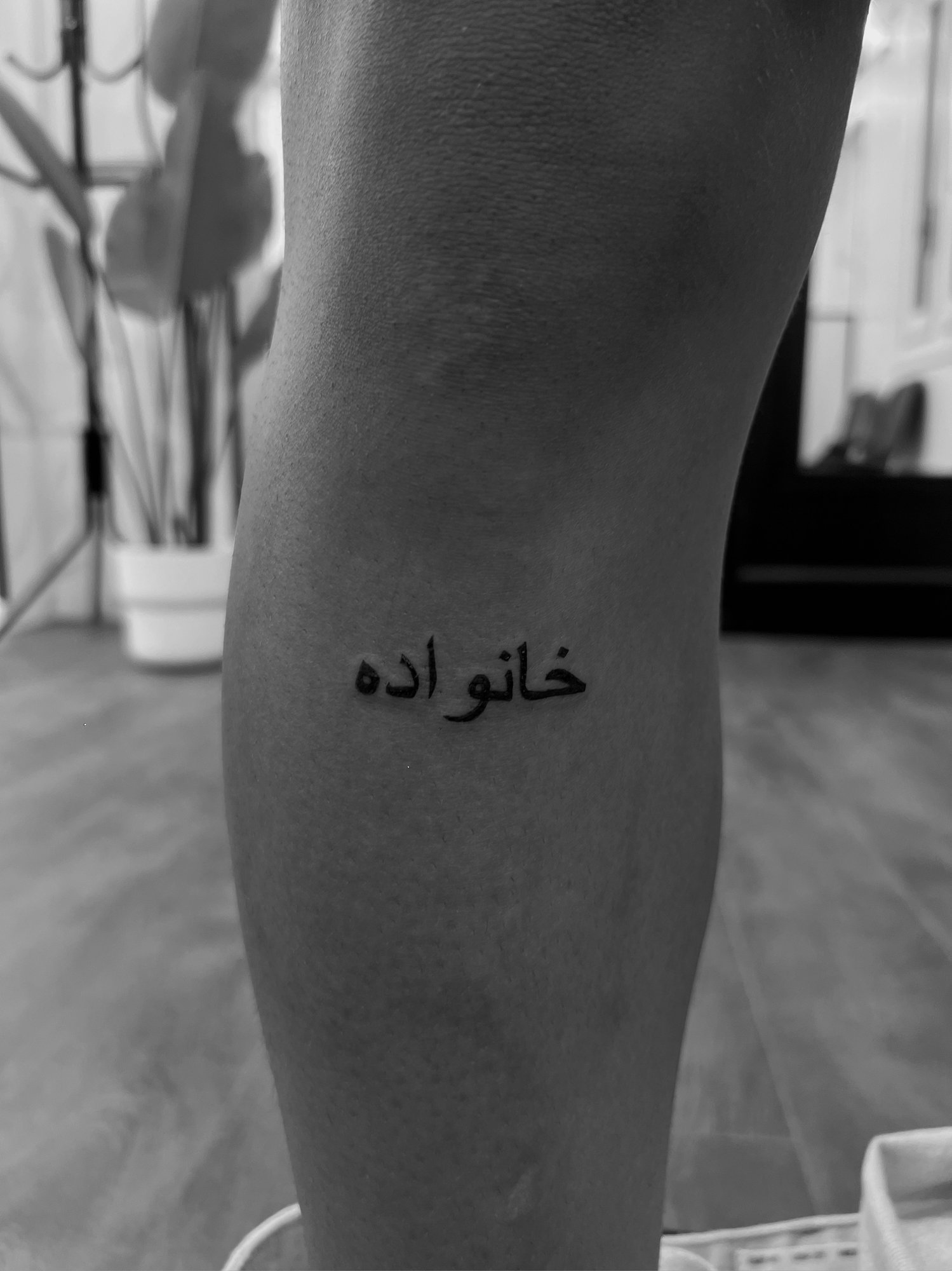 Tatuaje de palabra persa khanavadeh famil en pierna, línea fina