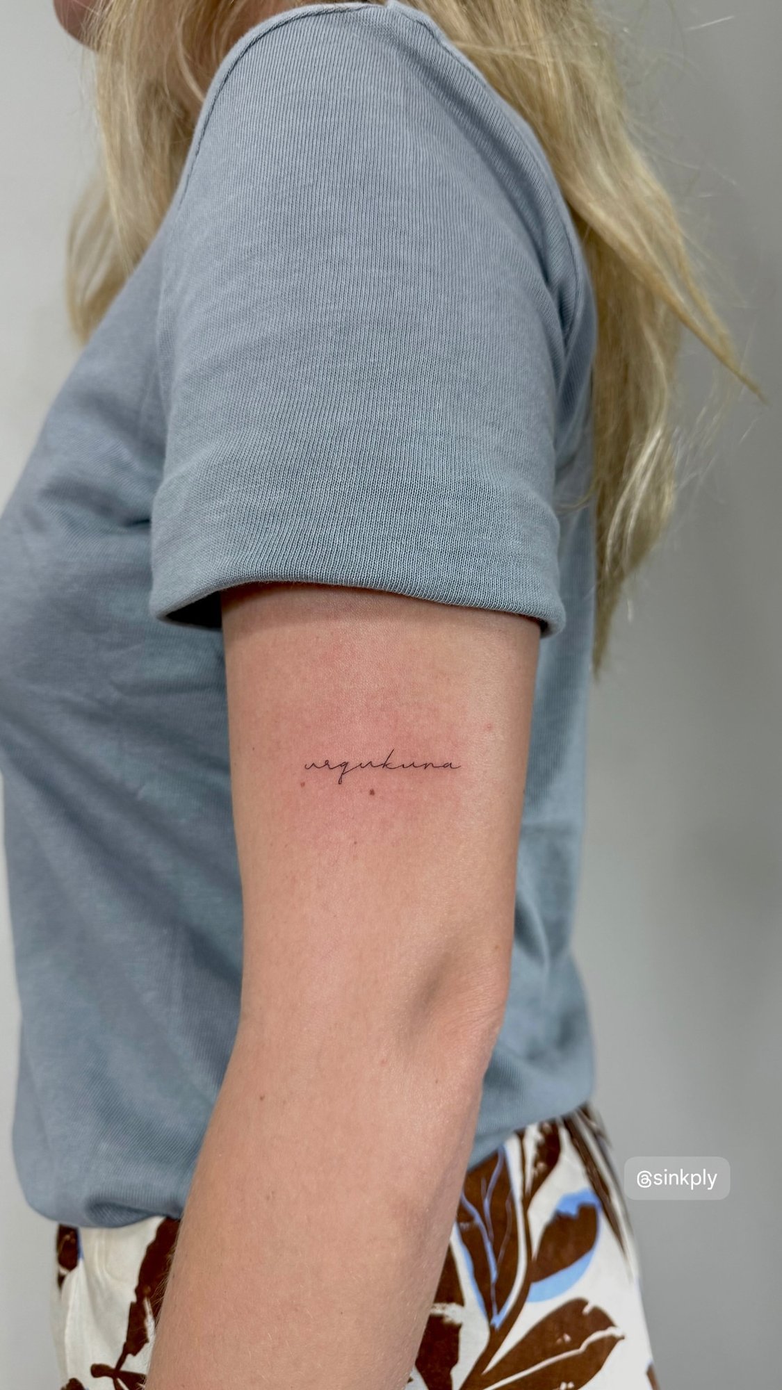 Tatuaje de palabra urqukuna caligrafia fi en brazo, línea fina