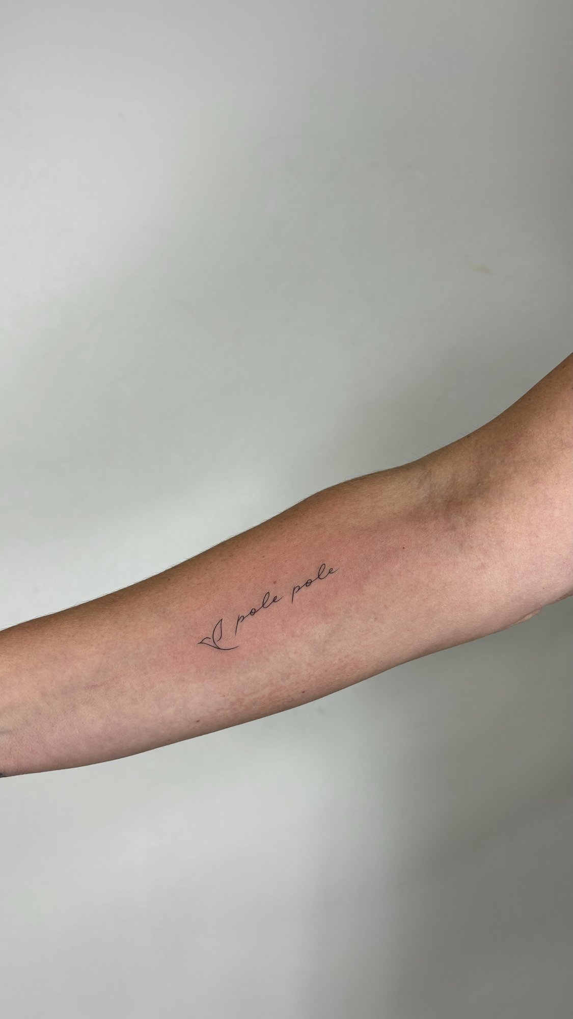 Tatuaje de pole pole caligrafia cursiva en antebrazo, línea fina
