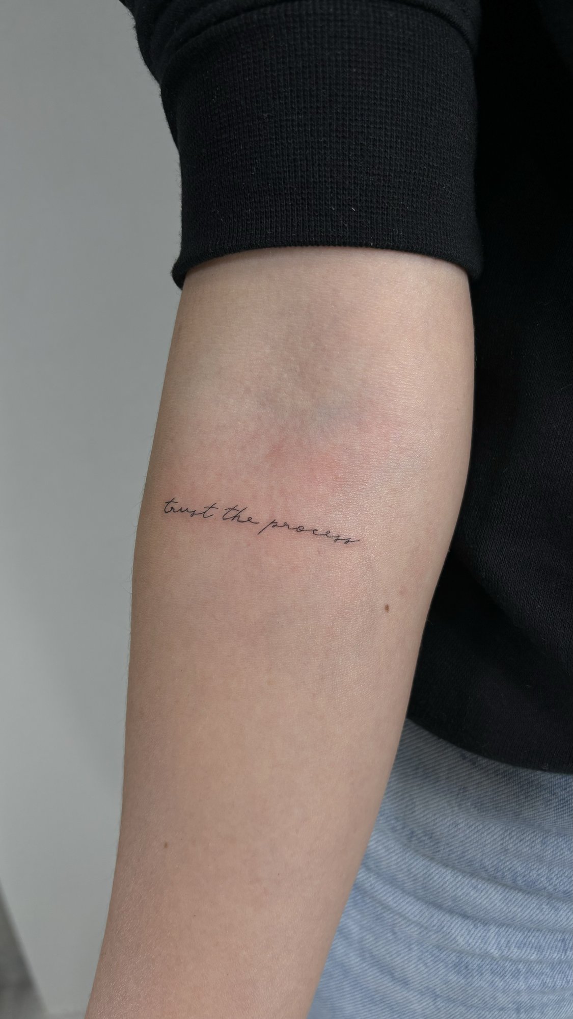 Tatuaje de trust the process cursiva en antebrazo, línea fina