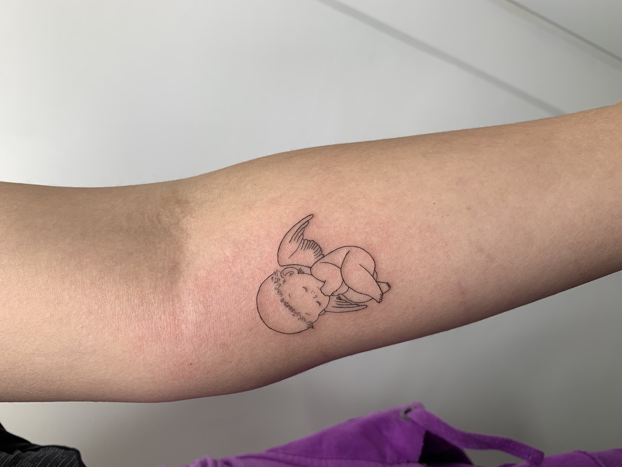 Tatuaje de bebe angel durmiendo alas en antebrazo, línea fina