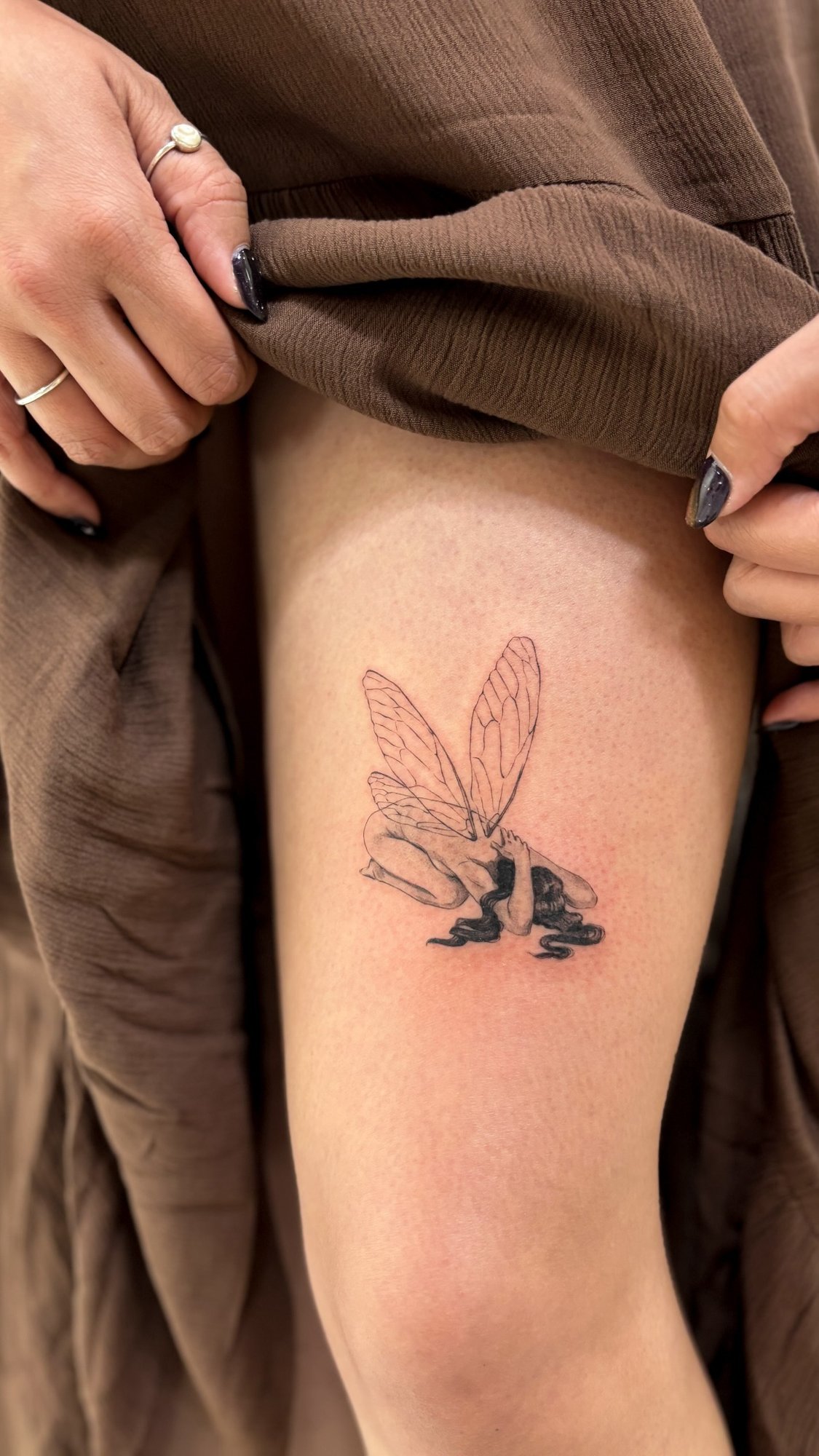 Tatuaje de hada caida con alas en muslo, línea fina