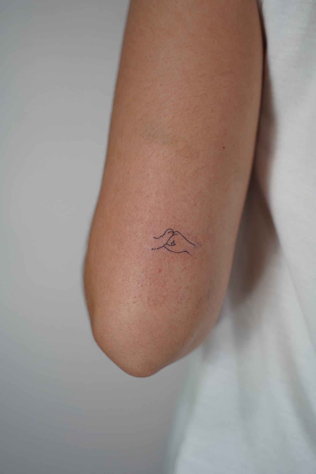 Tatuaje de manos formando corazon minimal en antebrazo, línea fina
