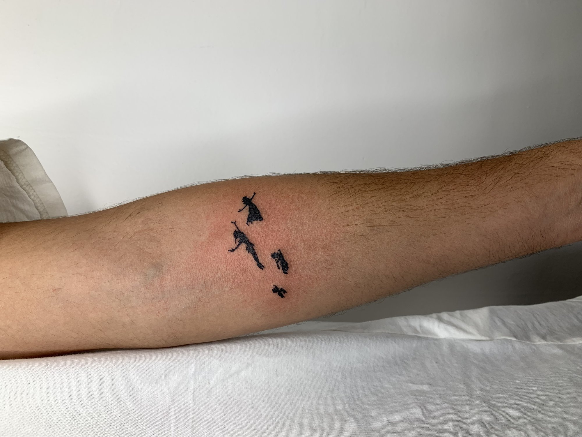 Tatuaje de siluetas peter pan volando en antebrazo, línea fina