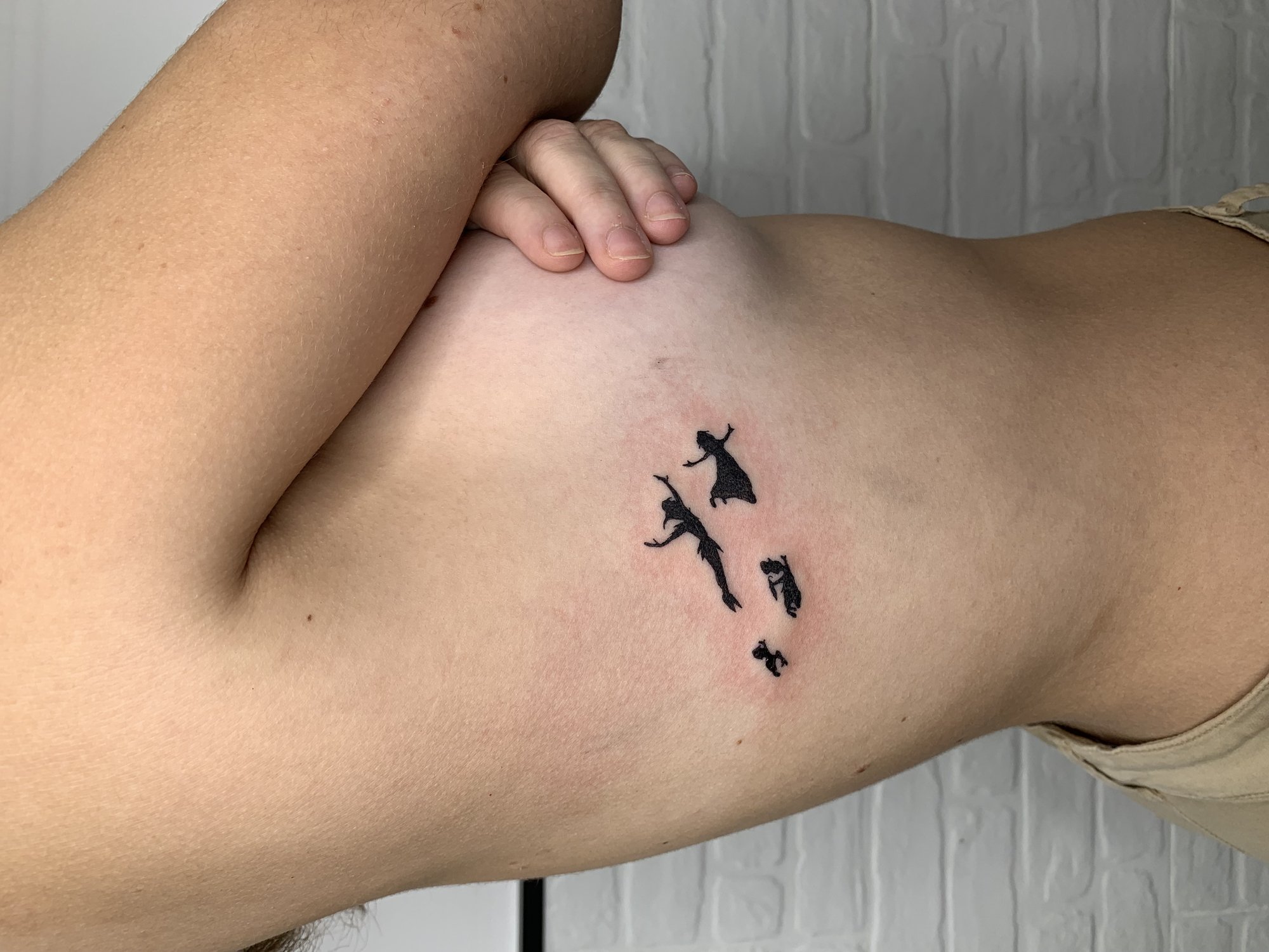 Tatuaje de siluetas peter pan volando en costilla, línea fina