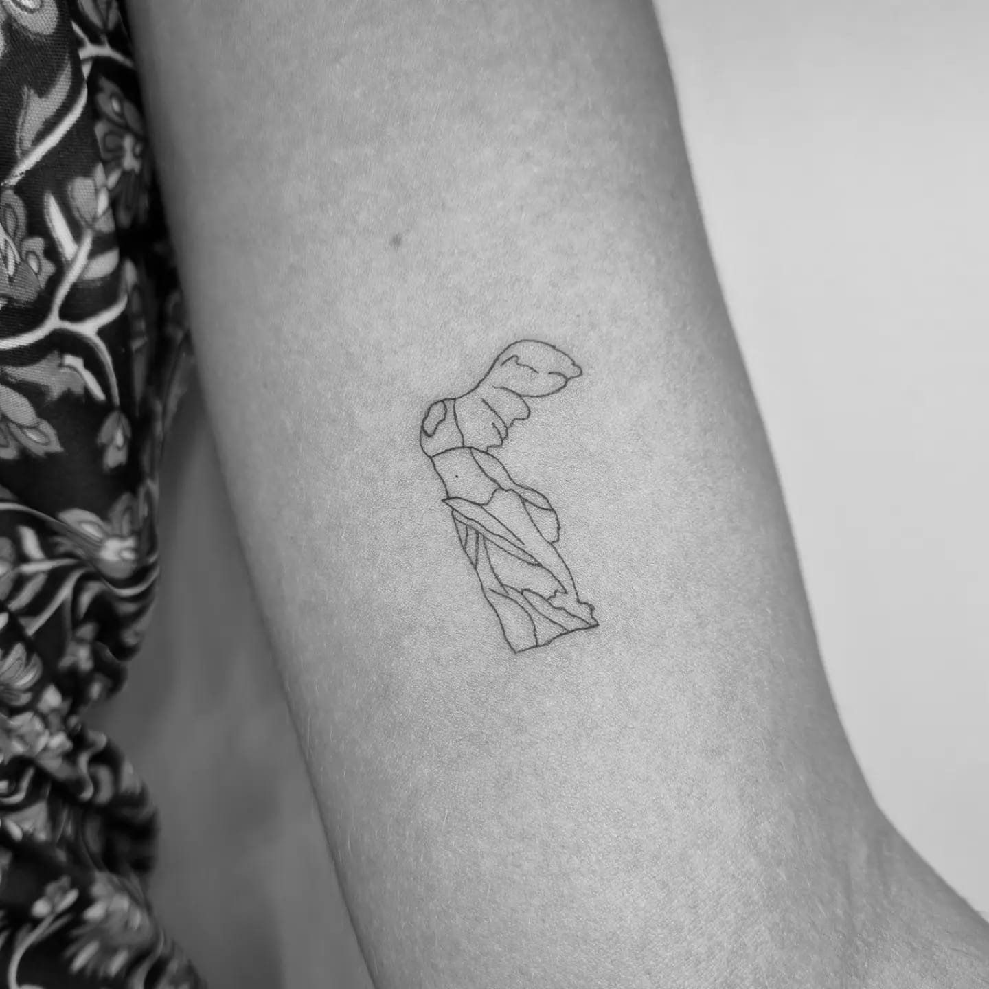 Tatuaje de venus de milo minimalista en brazo, línea fina