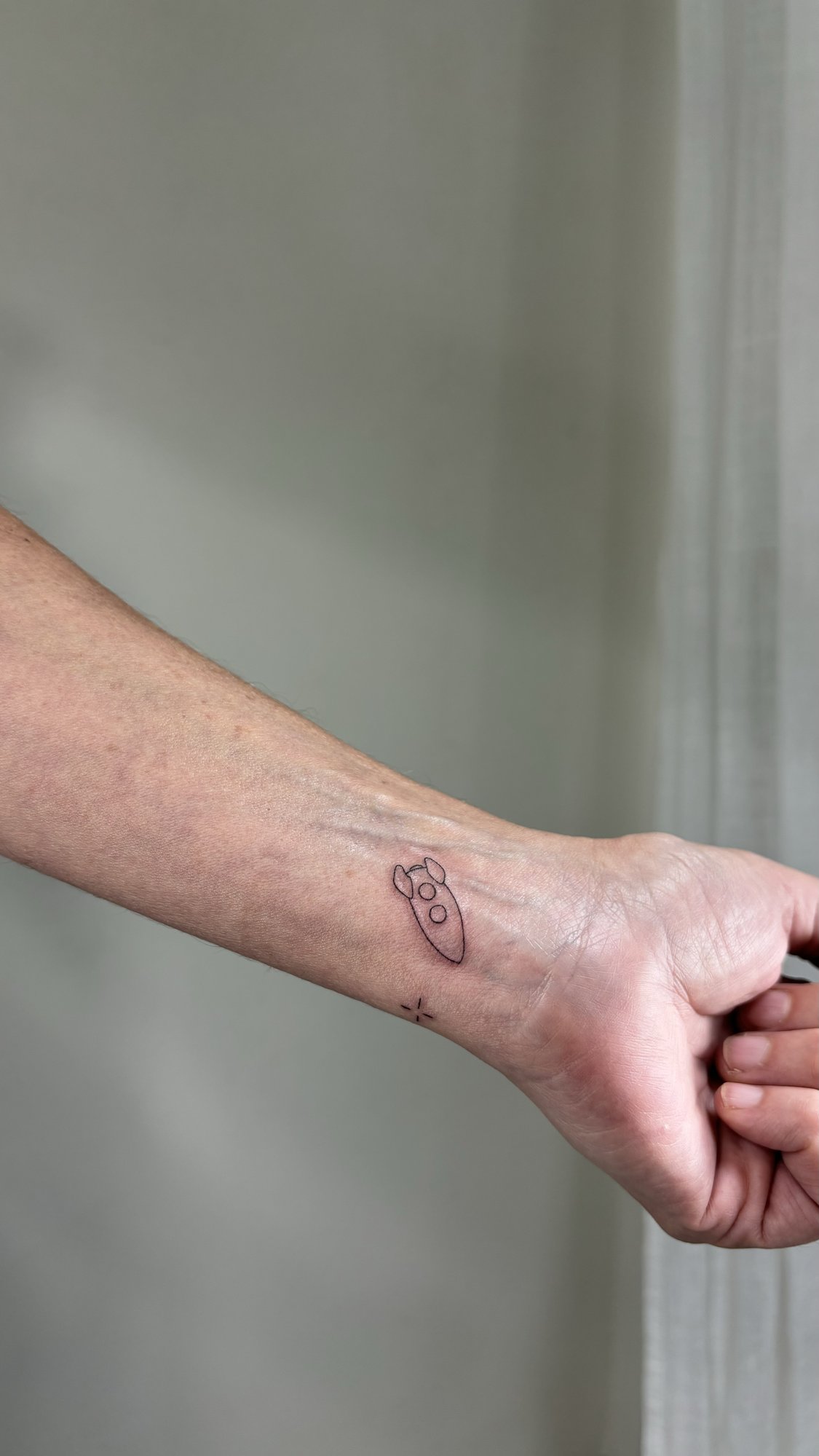 Tatuaje de cohete espacial con estrella en muneca, línea fina