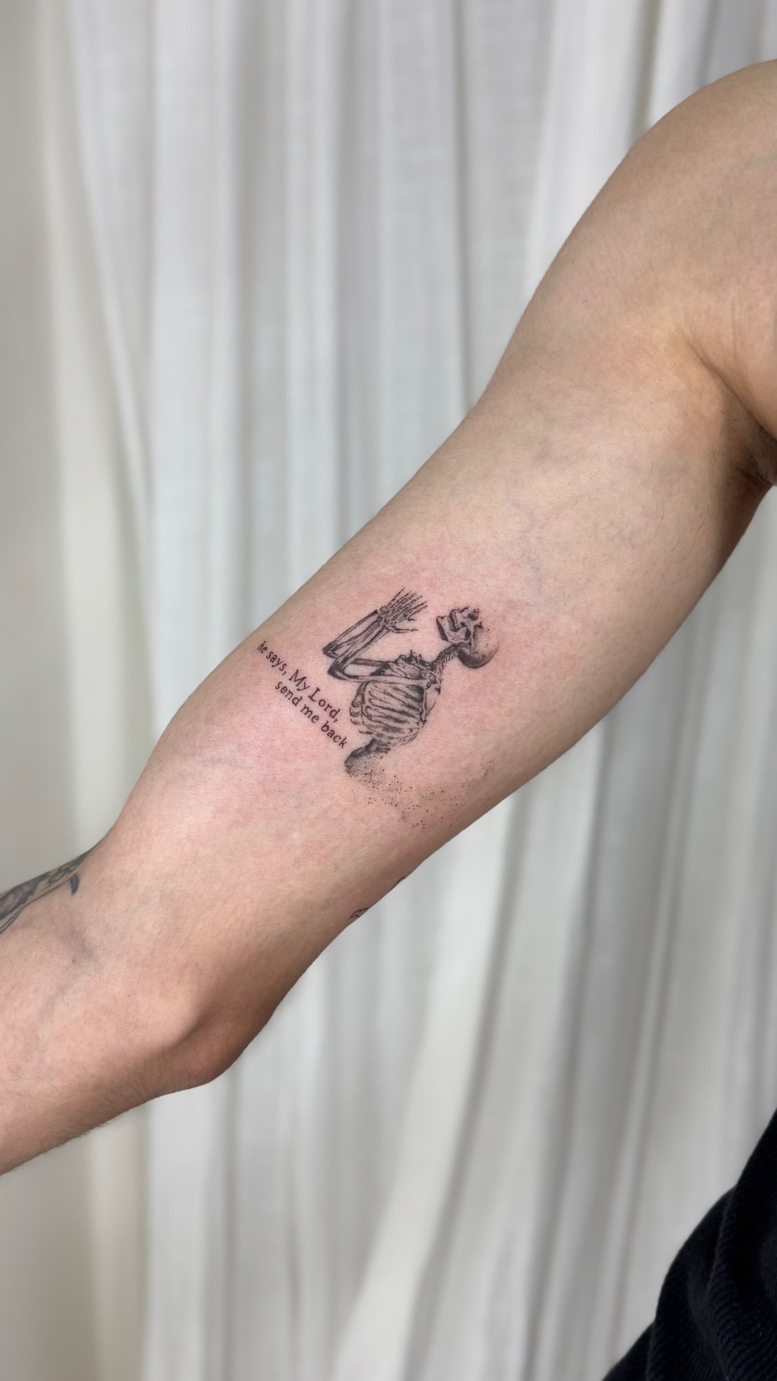 Tatuaje de esqueleto rezando con frase en brazo, línea fina