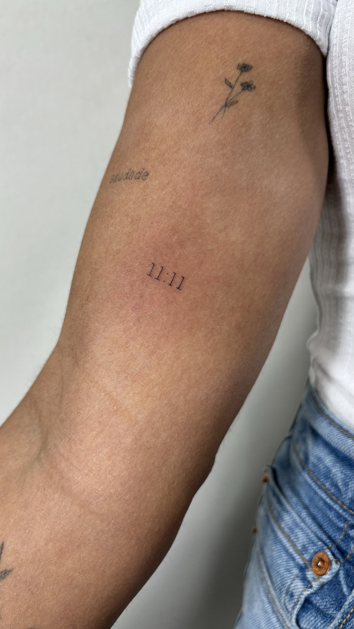 Tatuaje de flores saudade y 11:11 en brazo, línea fina