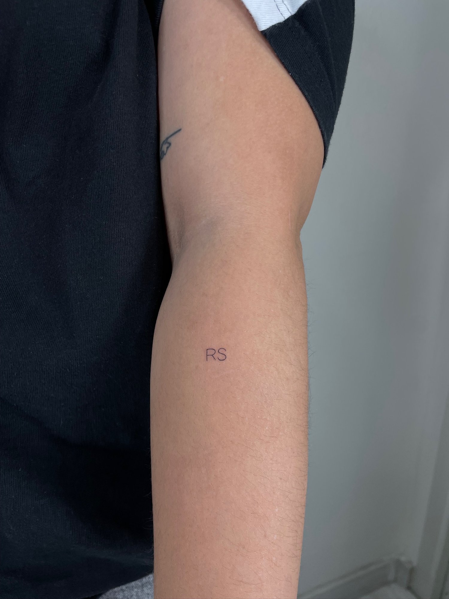 Tatuaje de iniciales rs y otro tattoo en brazo, línea fina