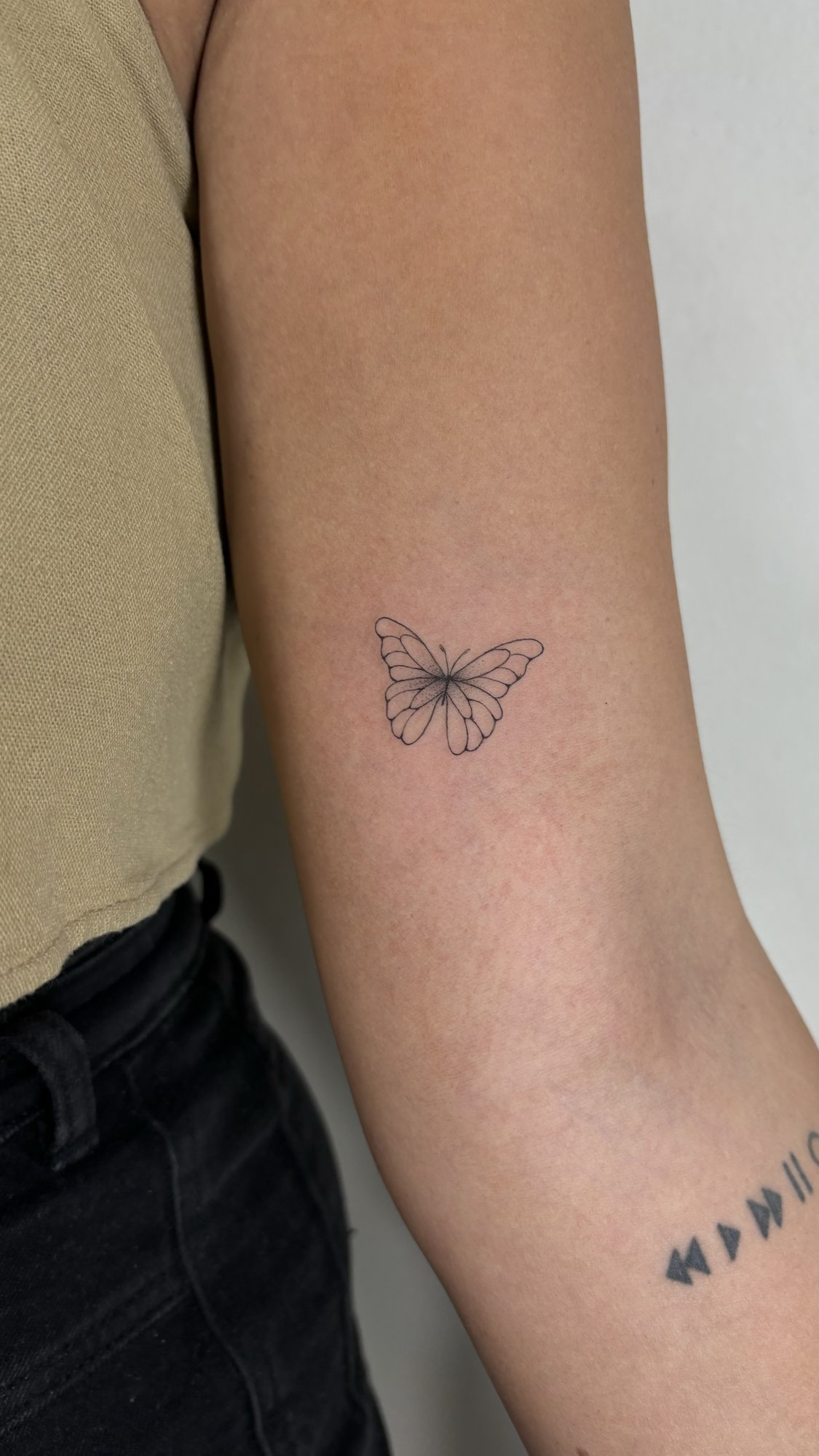 Tatuaje de mariposa fineline y simbolos en brazo, línea fina